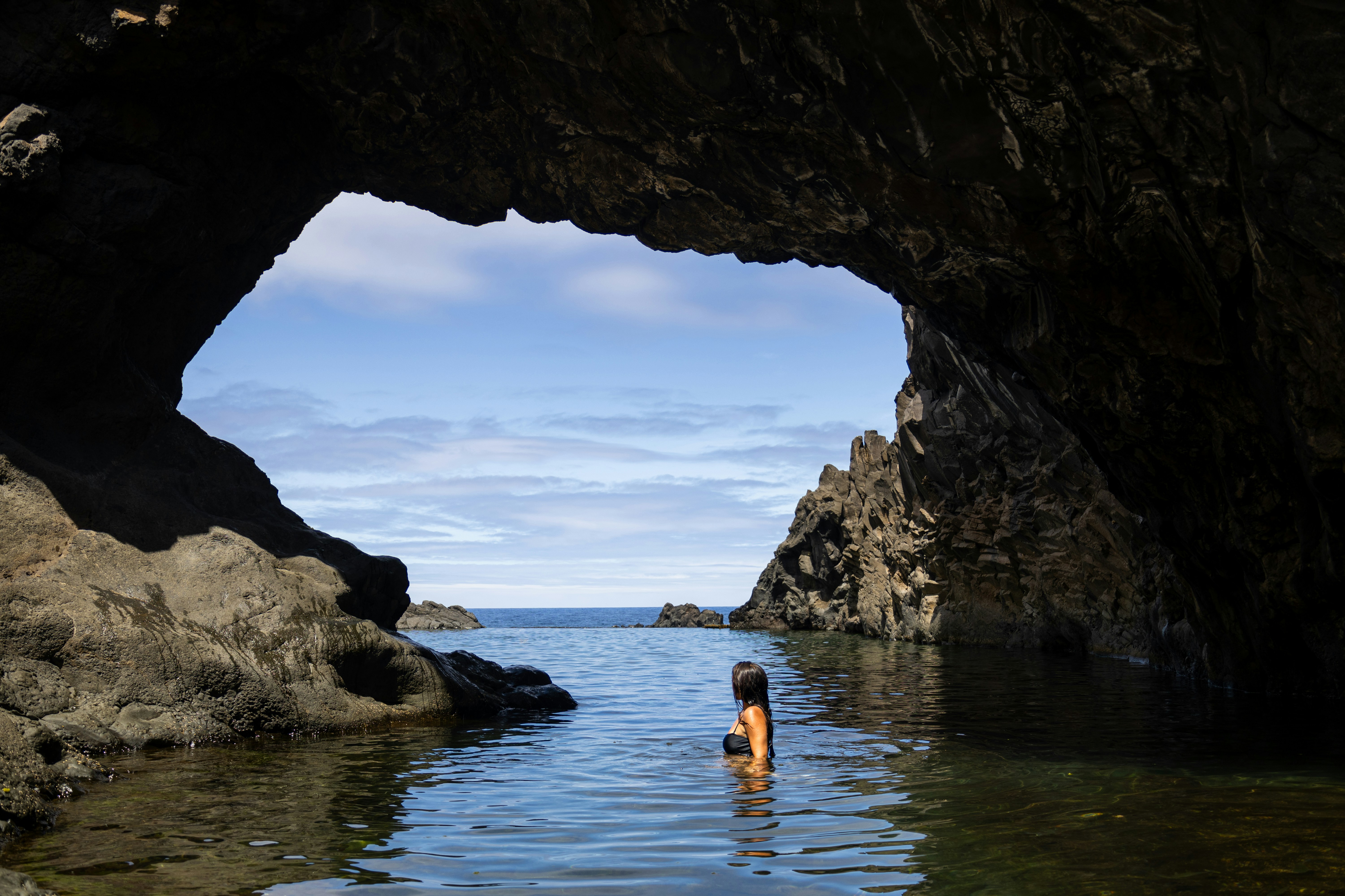 A person standing in a body of water under a cave