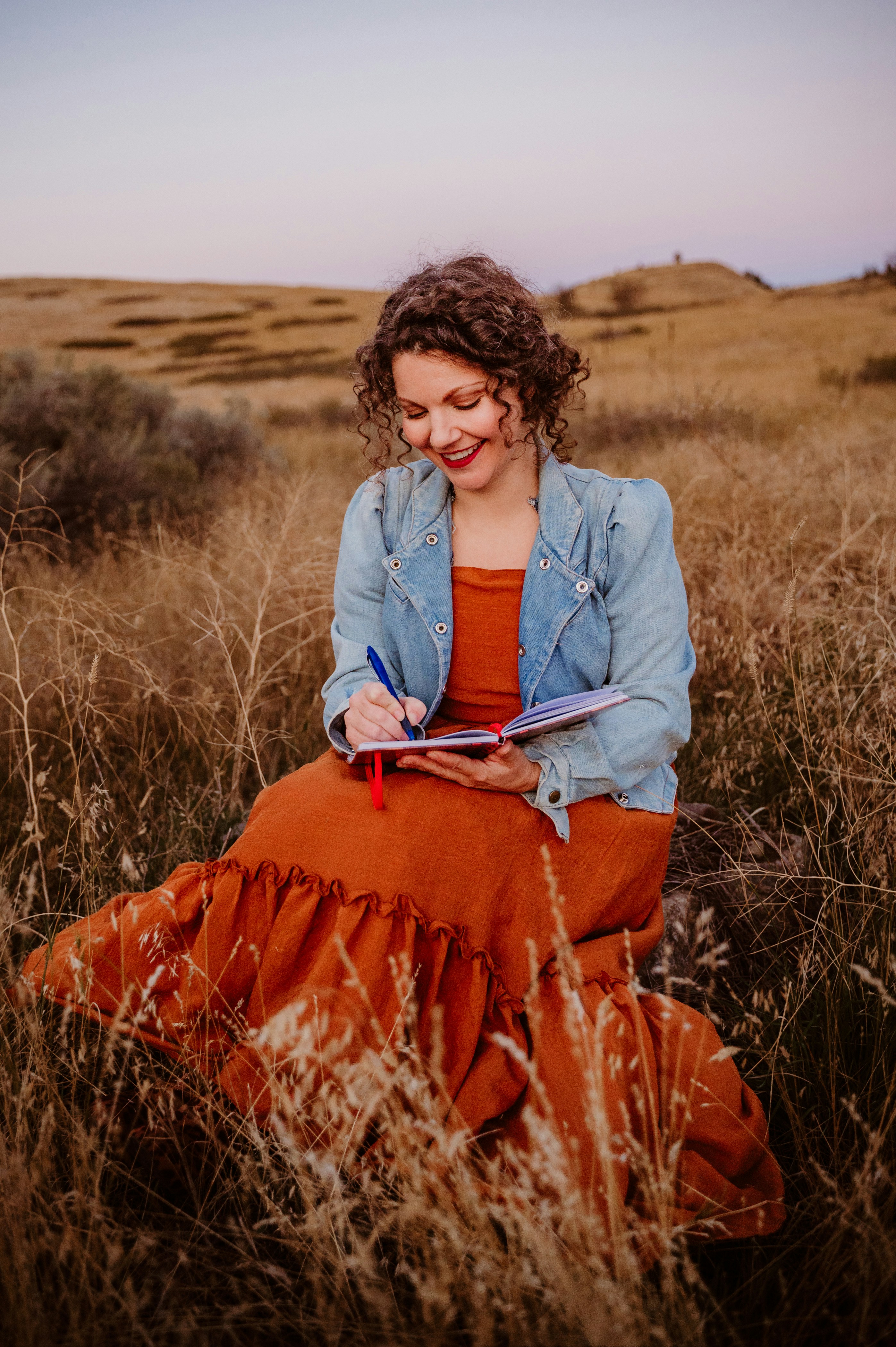 A woman sitting in a field writing on a notebook