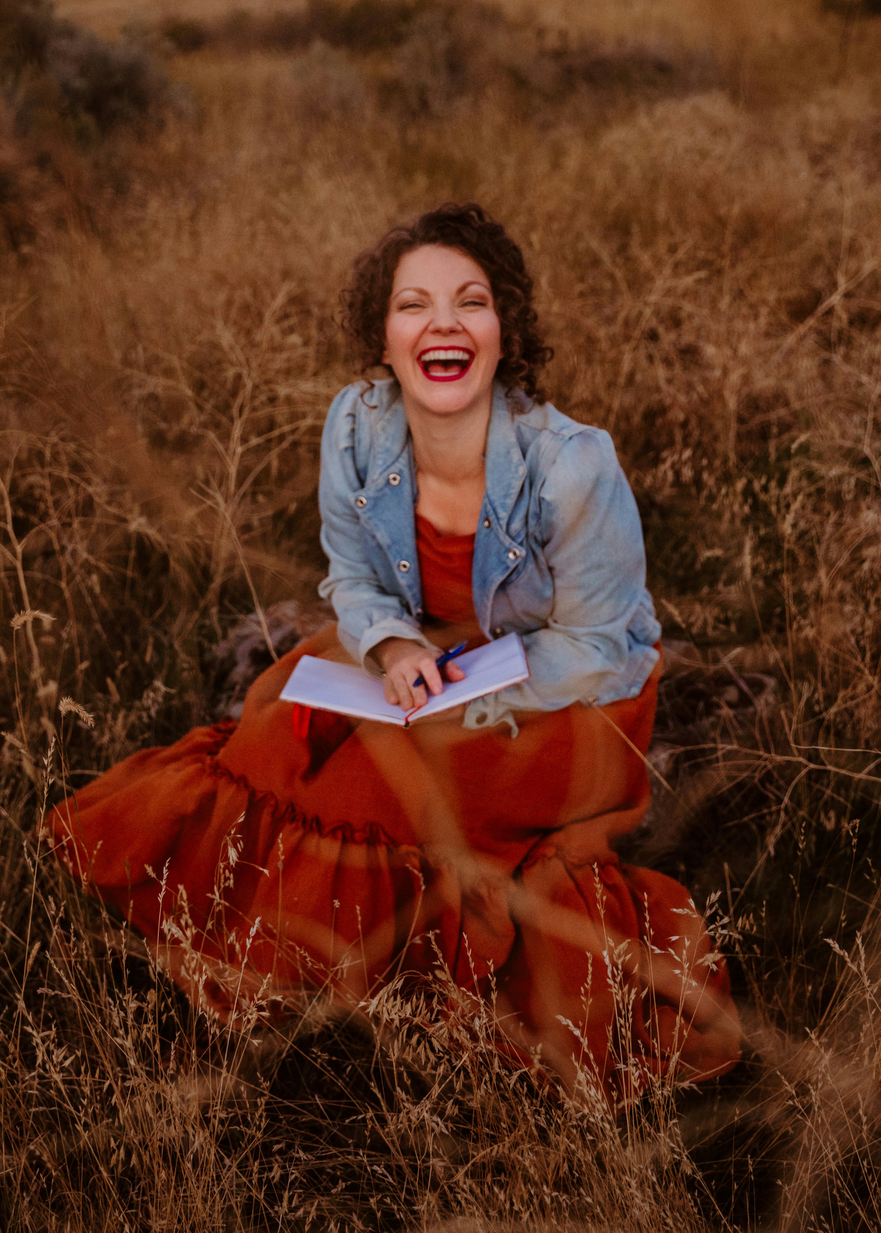 A woman sitting in a field laughing and holding a book