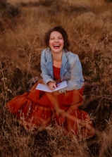 A woman sitting in a field laughing and holding a book