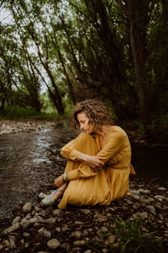 A woman in a yellow dress sitting on a river bank