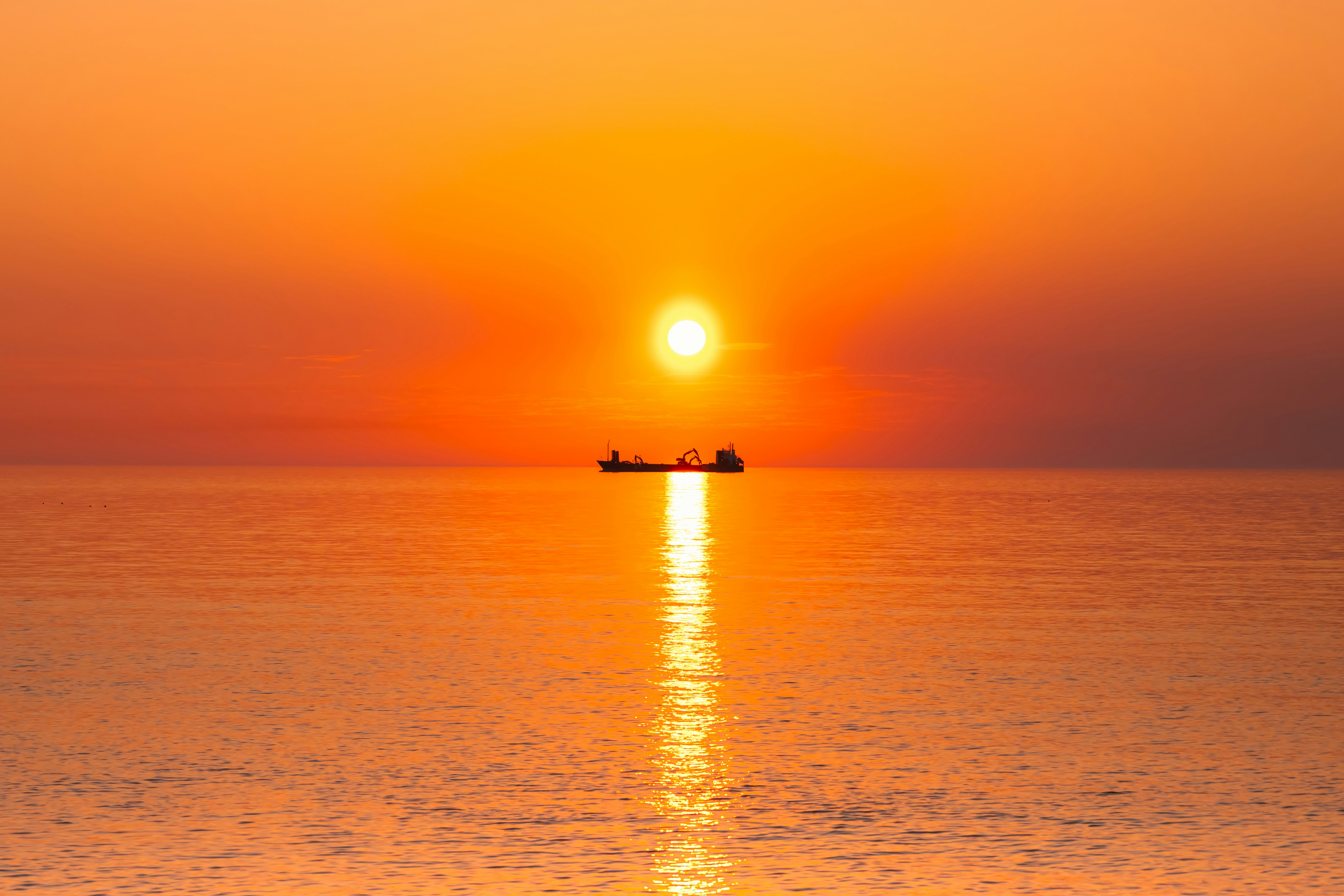 The sun is setting over the ocean with a boat in the distance