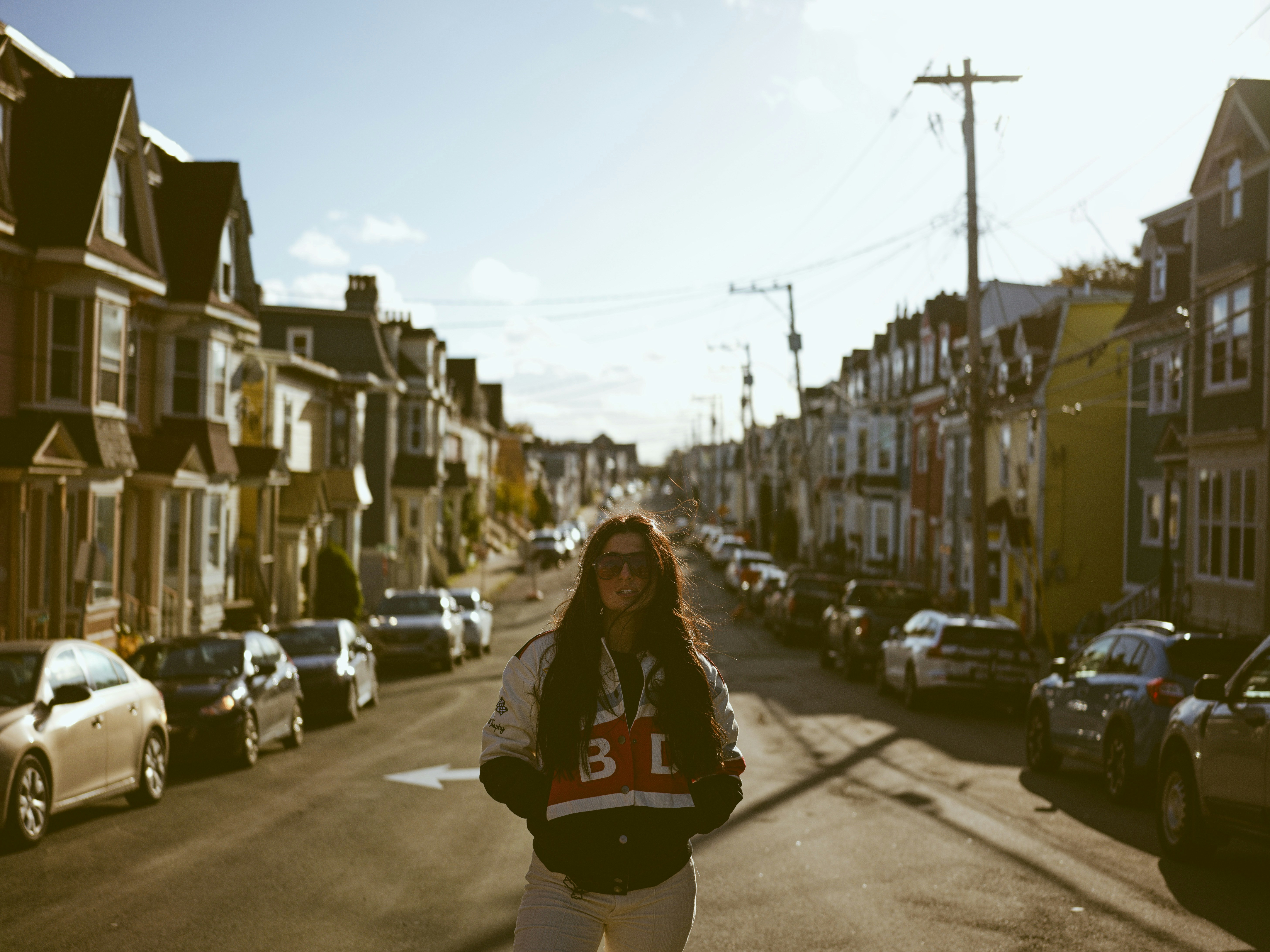 A woman walking down a street next to parked cars