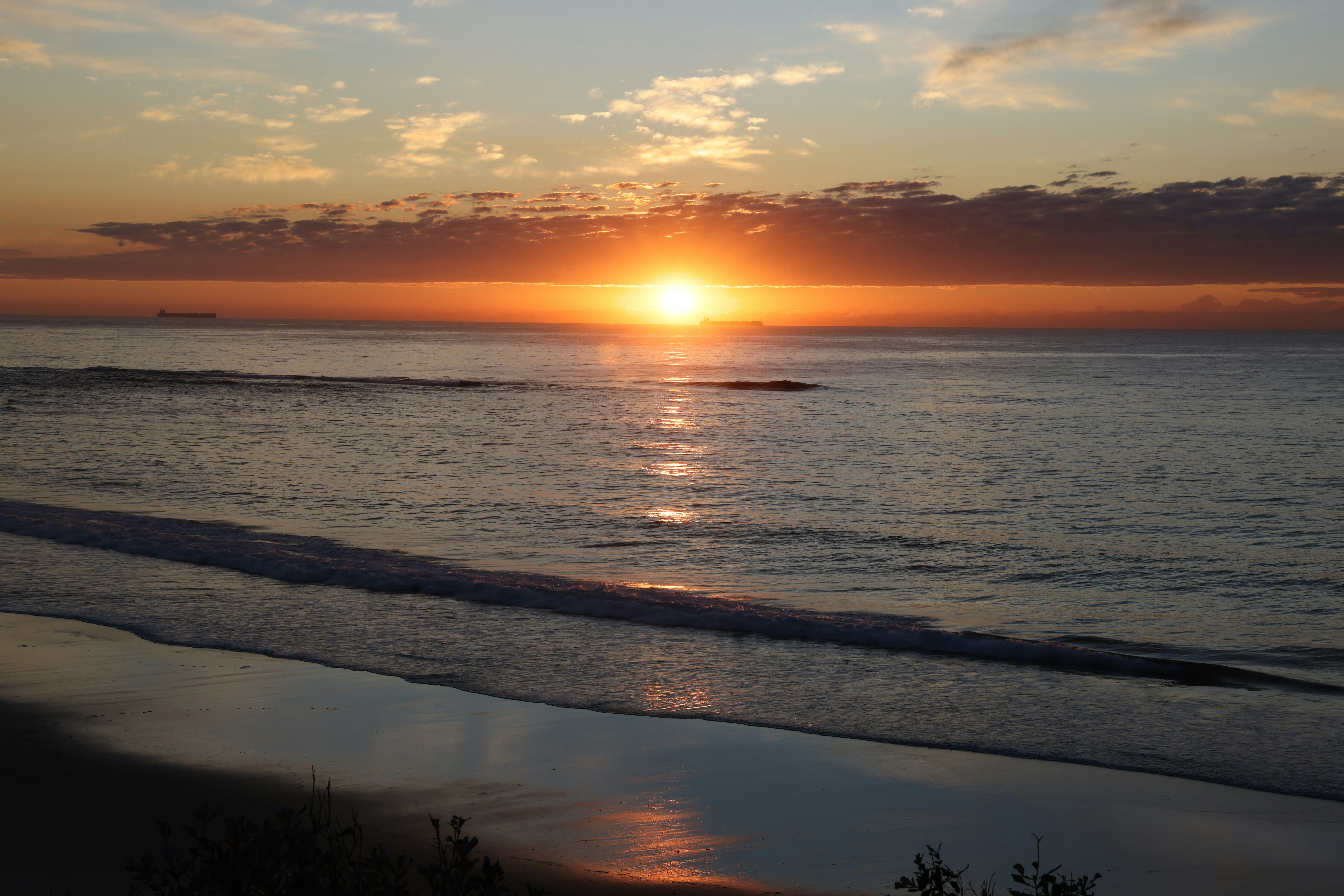 The sun is setting over the ocean on the beach