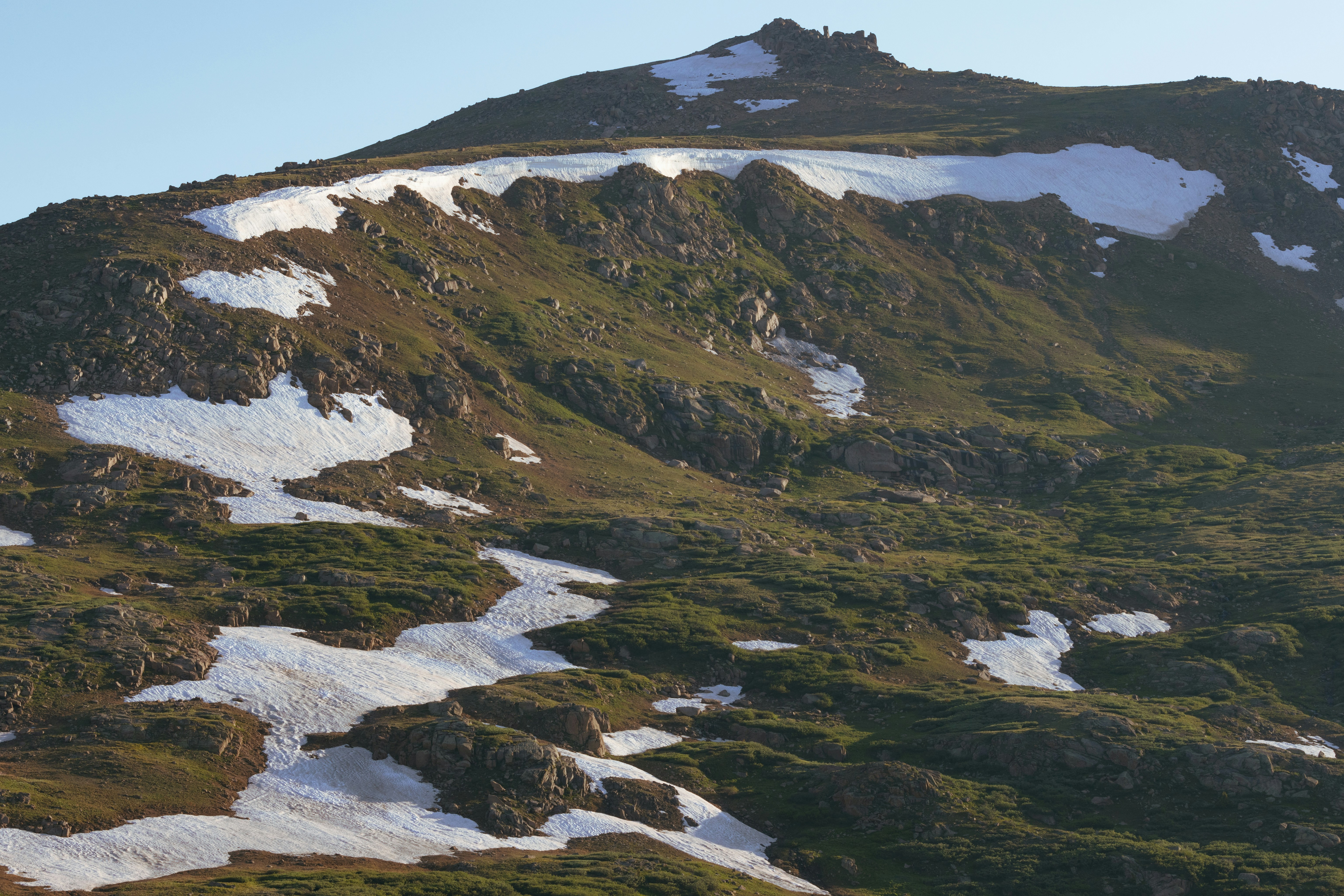 A mountain covered in snow and grass under a blue sky