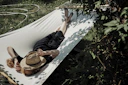 A man laying in a hammock with a hat on
