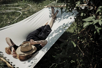A man laying in a hammock with a hat on
