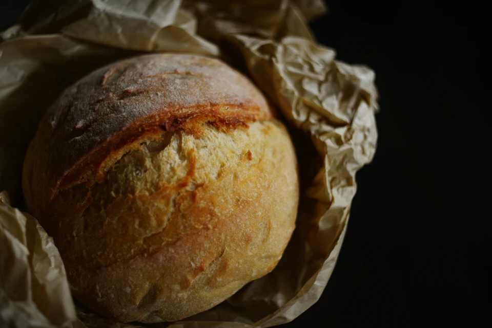 Freshly baked loaf of bread rests on parchment paper, showcasing its golden brown crust