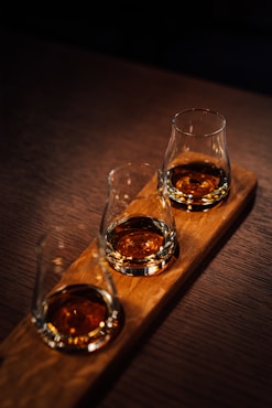 Three glasses of whiskey sitting on a wooden tray