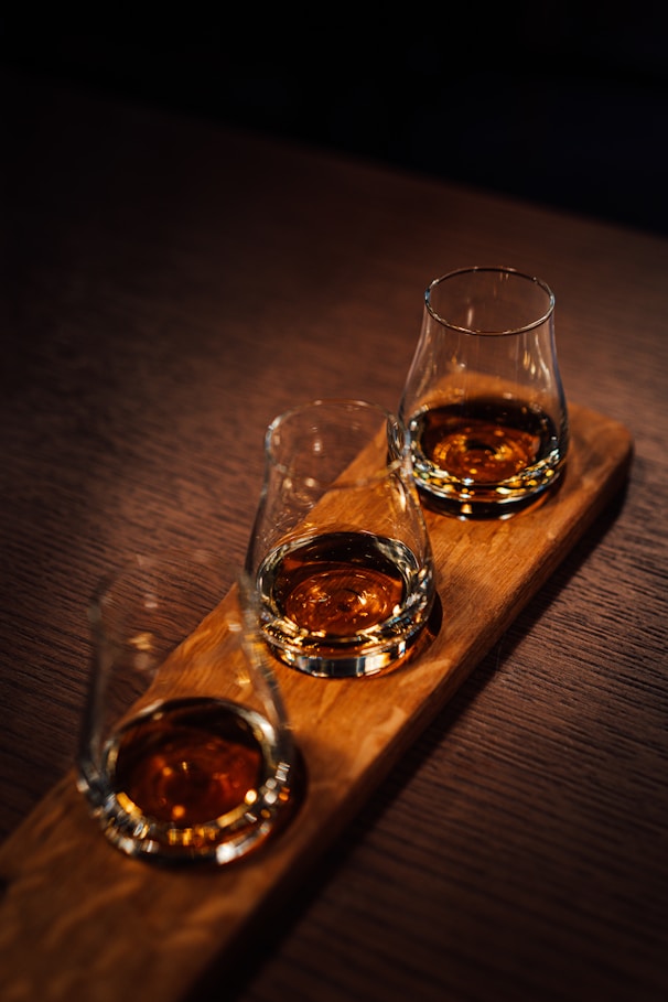 Three glasses of whiskey sitting on a wooden tray
