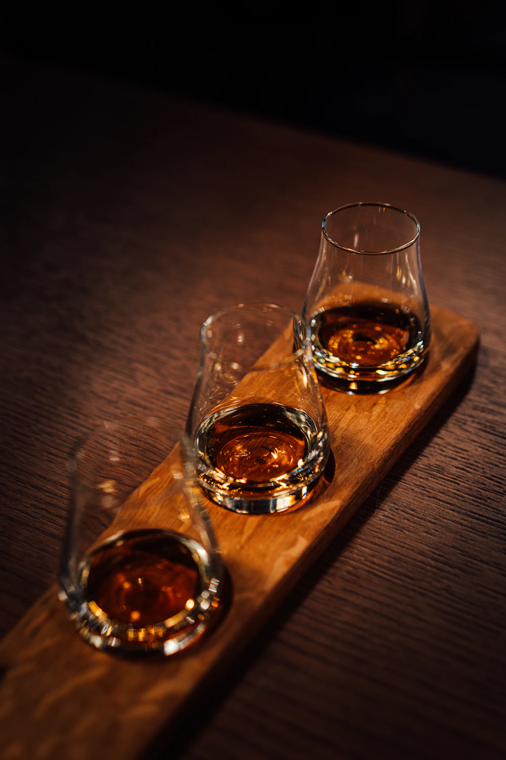 Flight of three whisky tasting glasses on a wooden tray