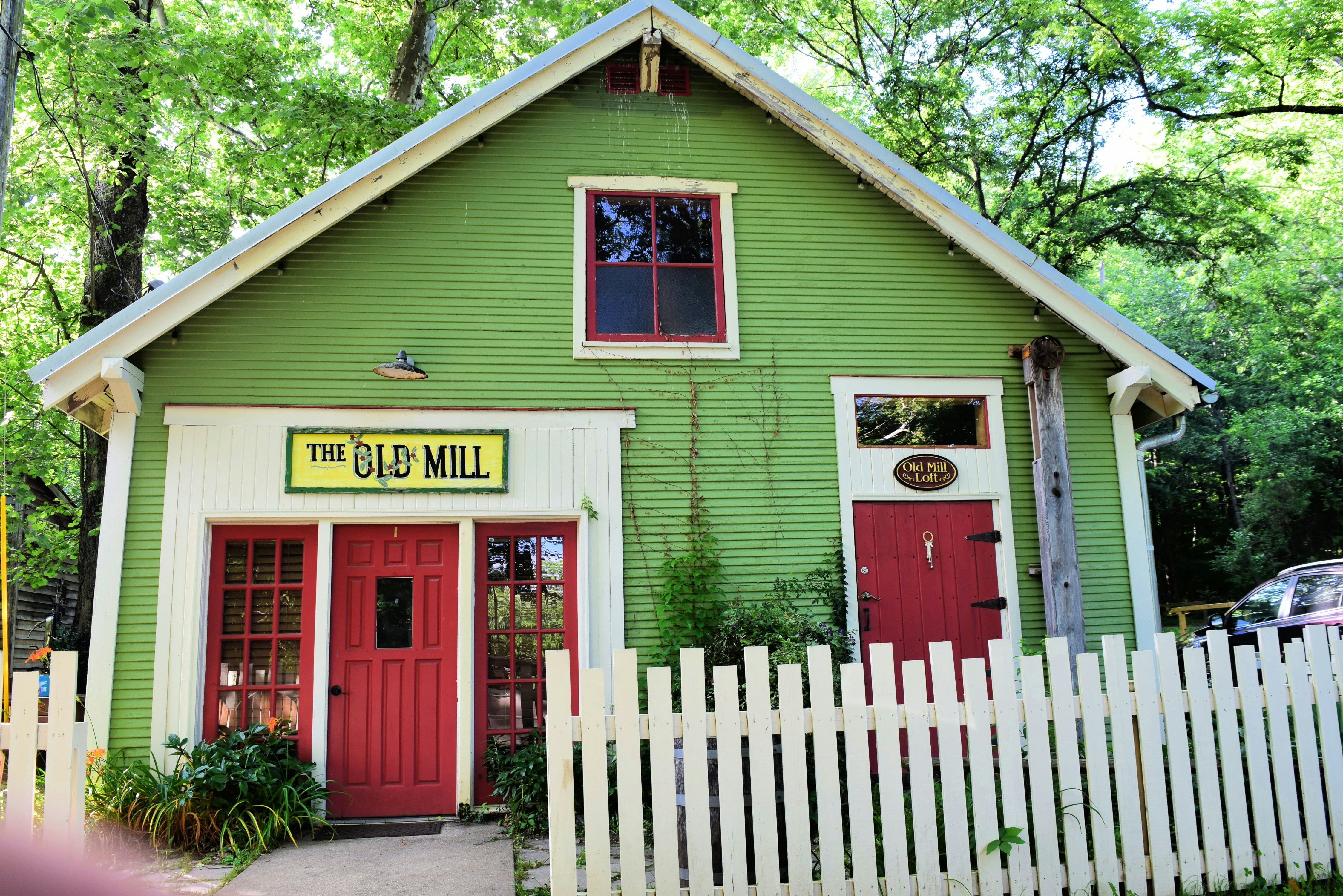 A small green building with red doors and a white picket fence