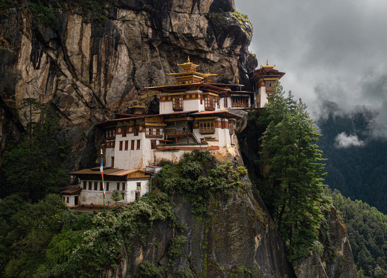 Taktsang monastery clinging to its granite cliff above Paro, gilded roofs over whitewashed walls and pines below