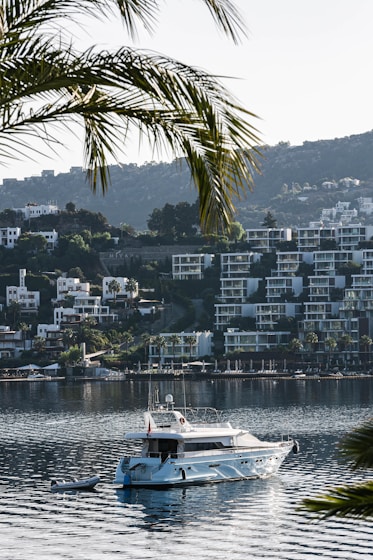 MG TURIZM A white boat in a body of water with a city in the background