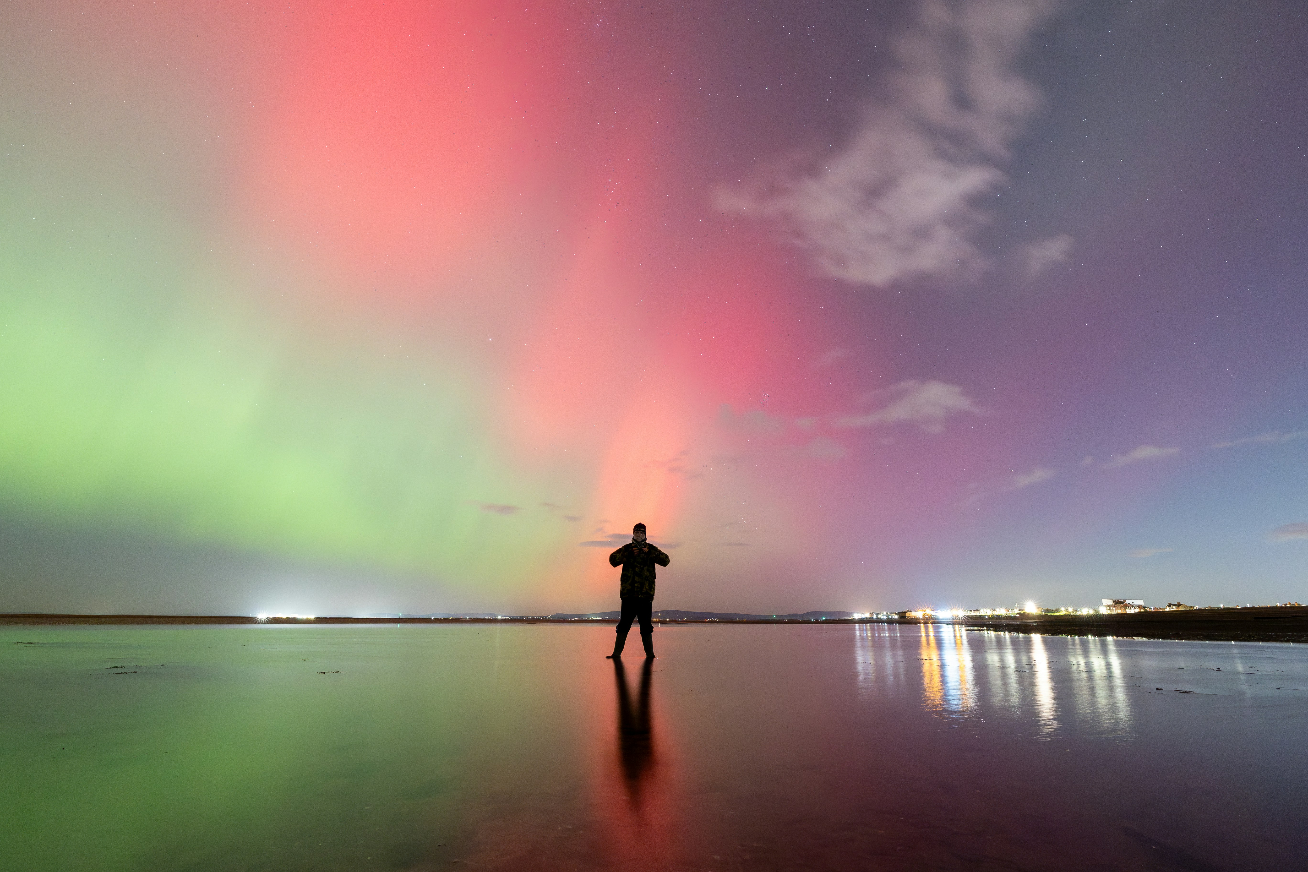 A man standing on a beach under a colorful sky