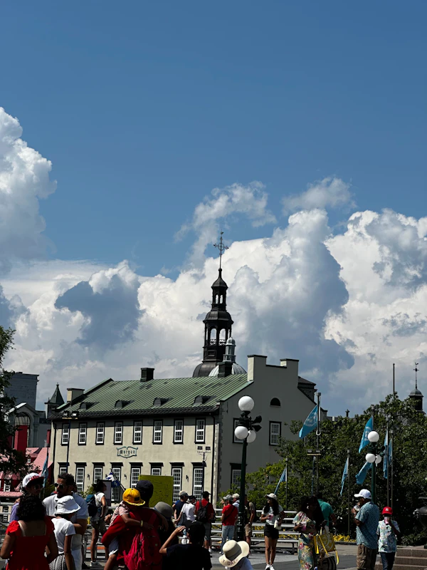 A crowd in a square beside an old stone building with a spire