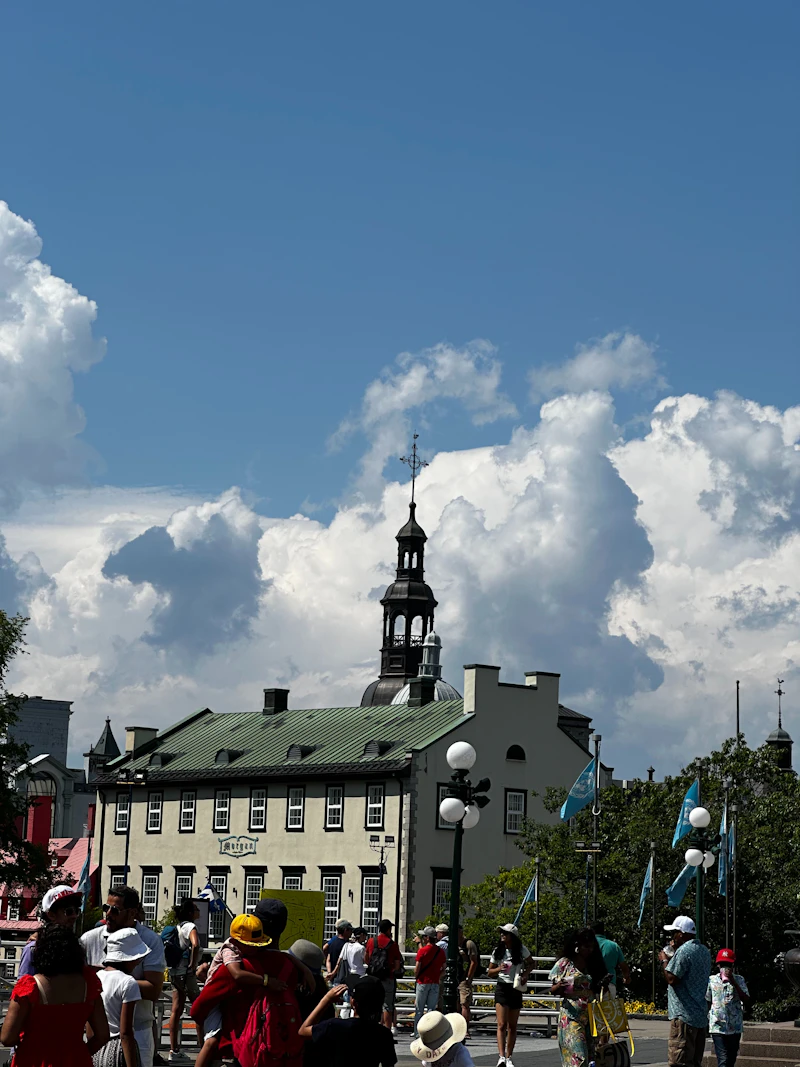 A crowd in a square beside an old stone building with a spire