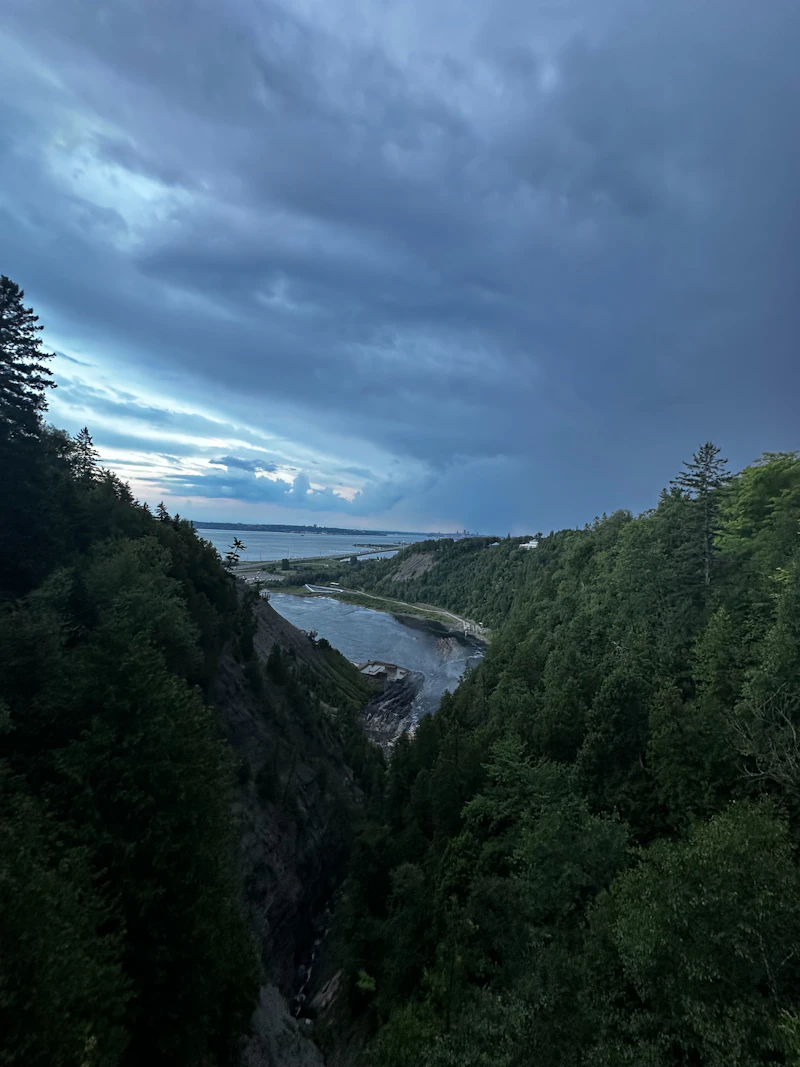 A river canyon between forested cliffs under a cloudy sky