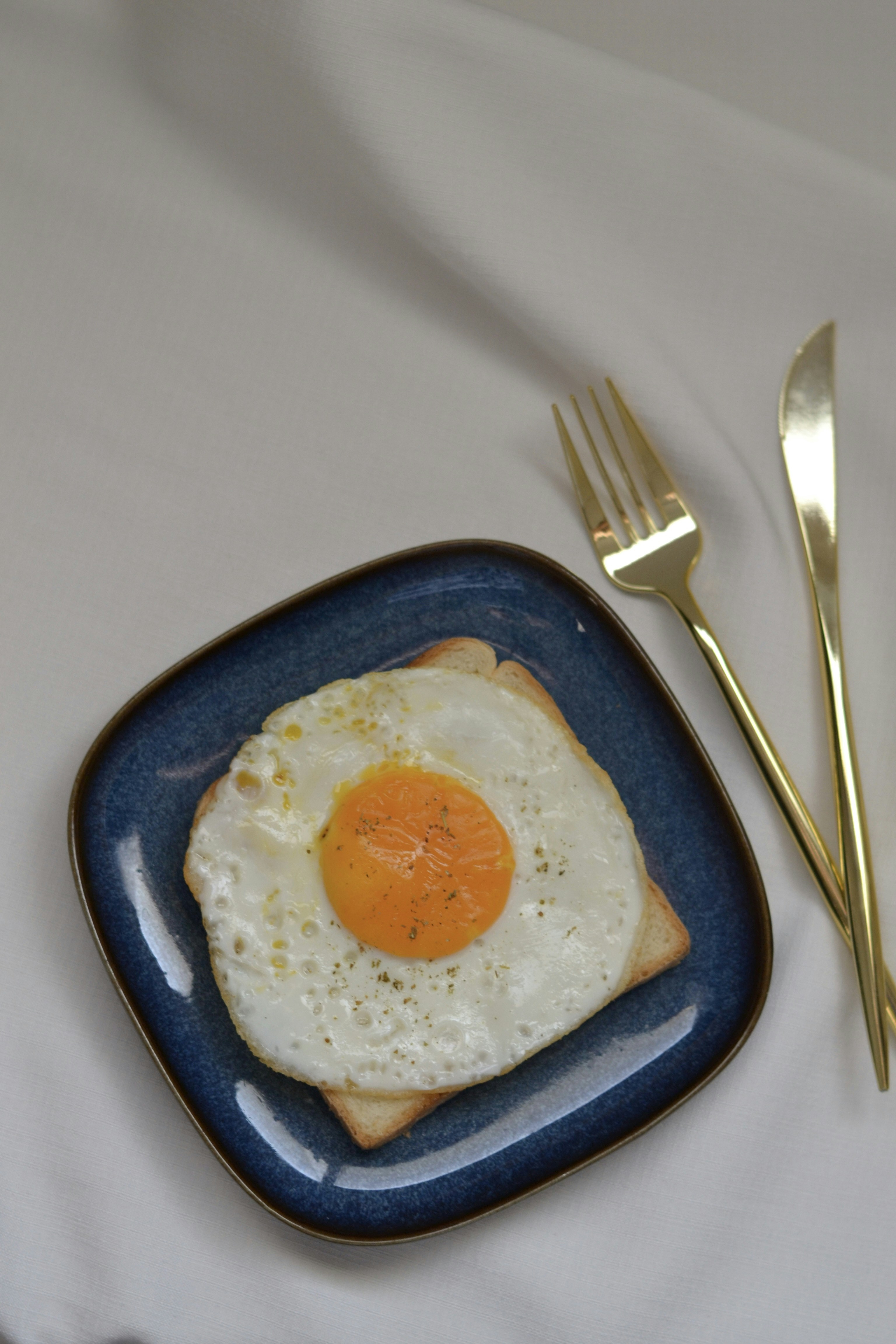 A plate with a fried egg on it next to a fork and knife