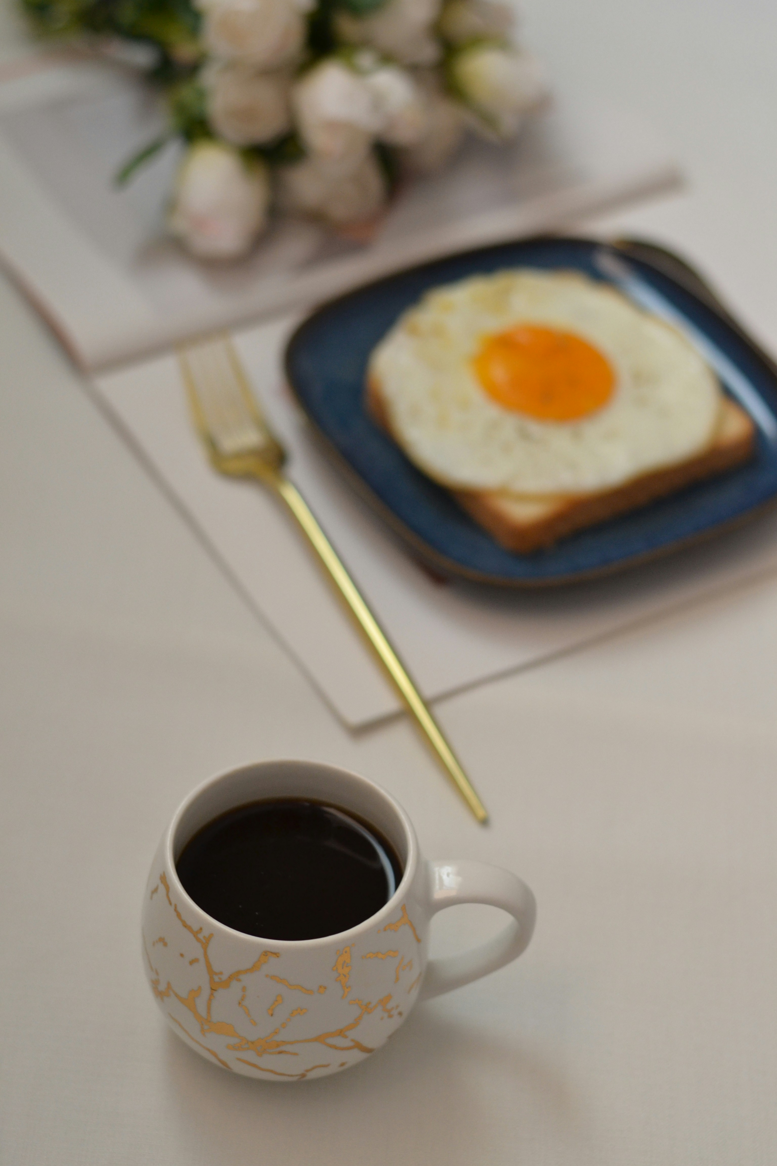 A cup of coffee next to a plate with an egg on it