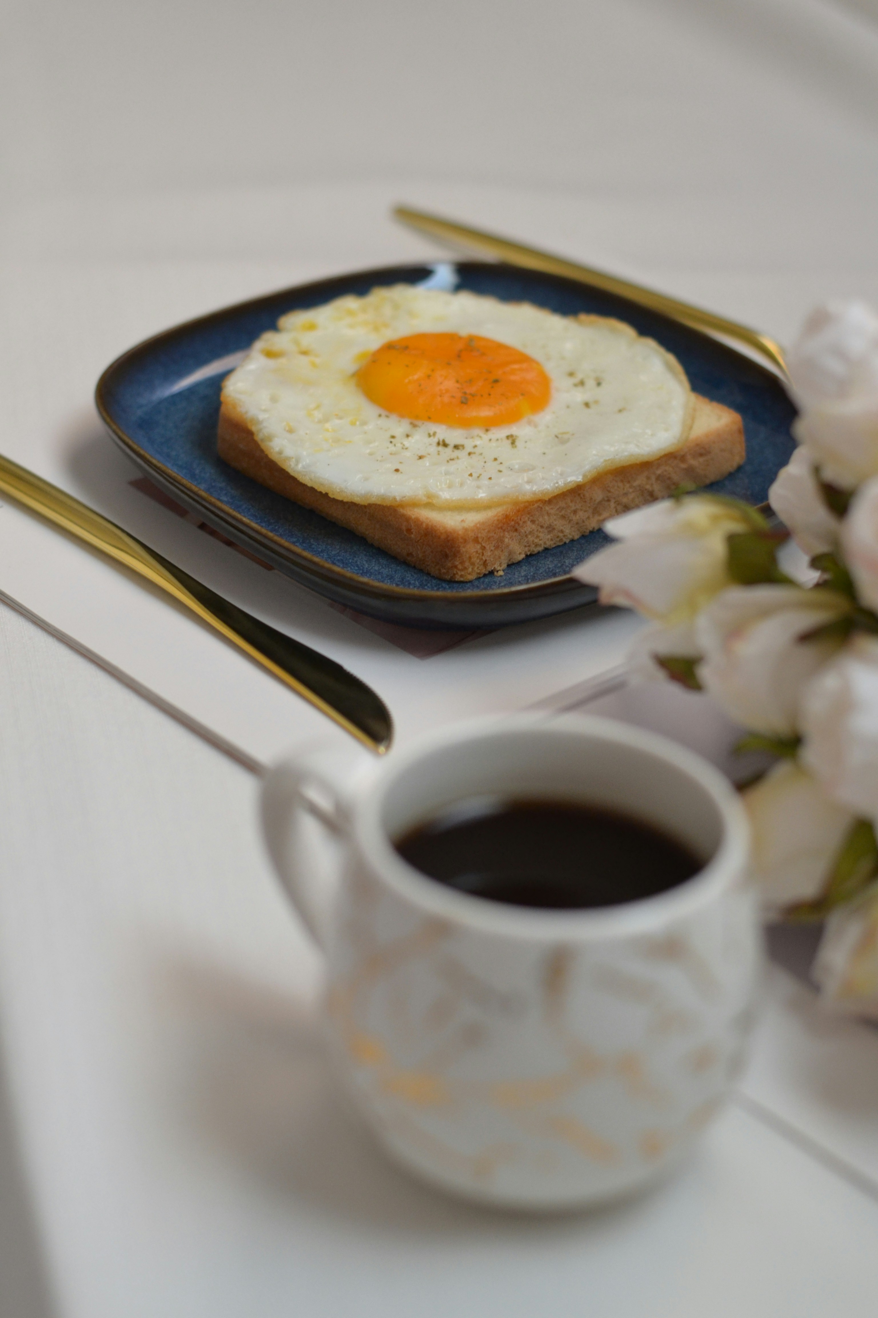 A cup of coffee next to a plate with an egg on it