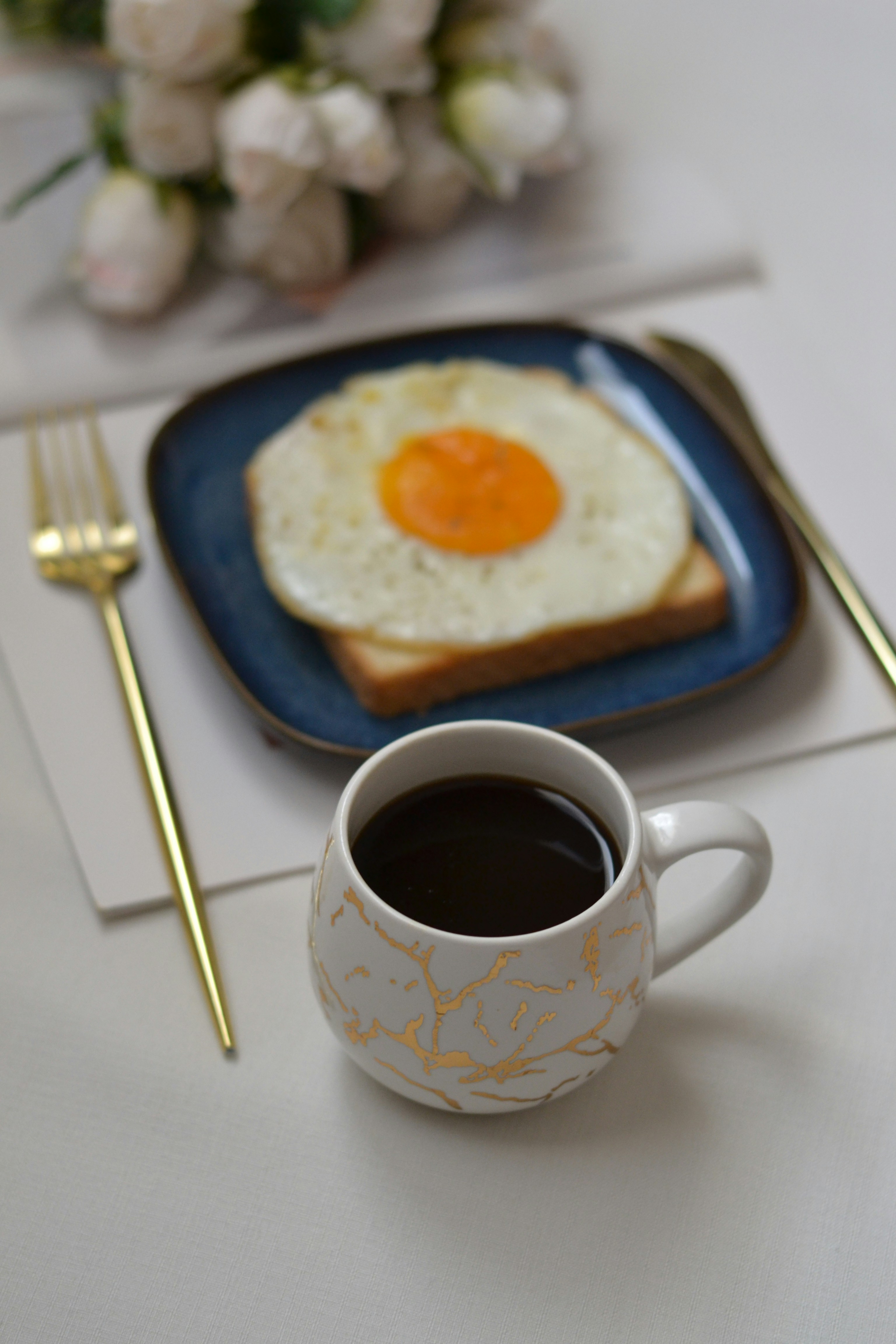 A cup of coffee next to a plate with an egg on it