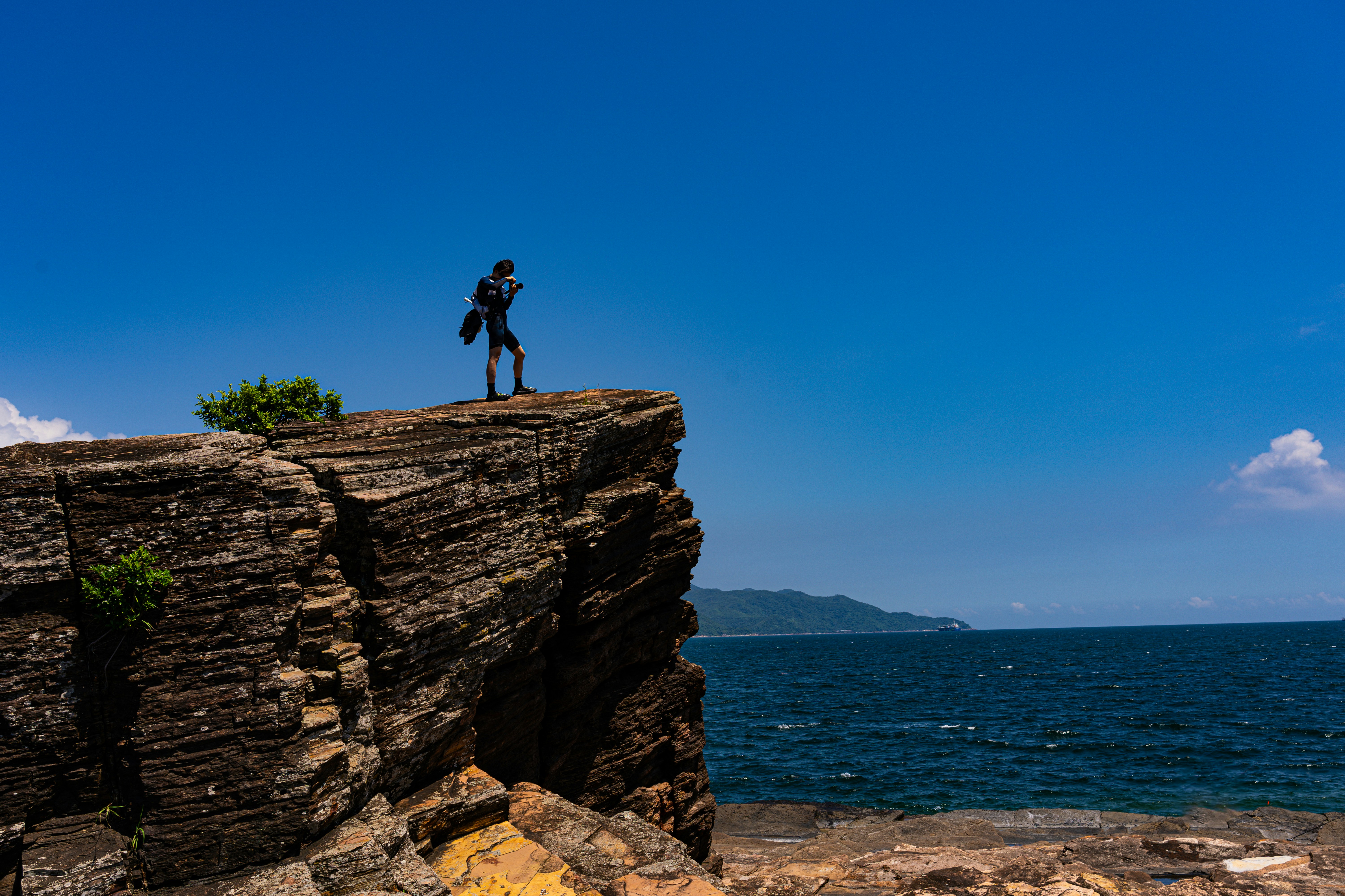 A man standing on top of a cliff next to the ocean photo – Free Photo ...