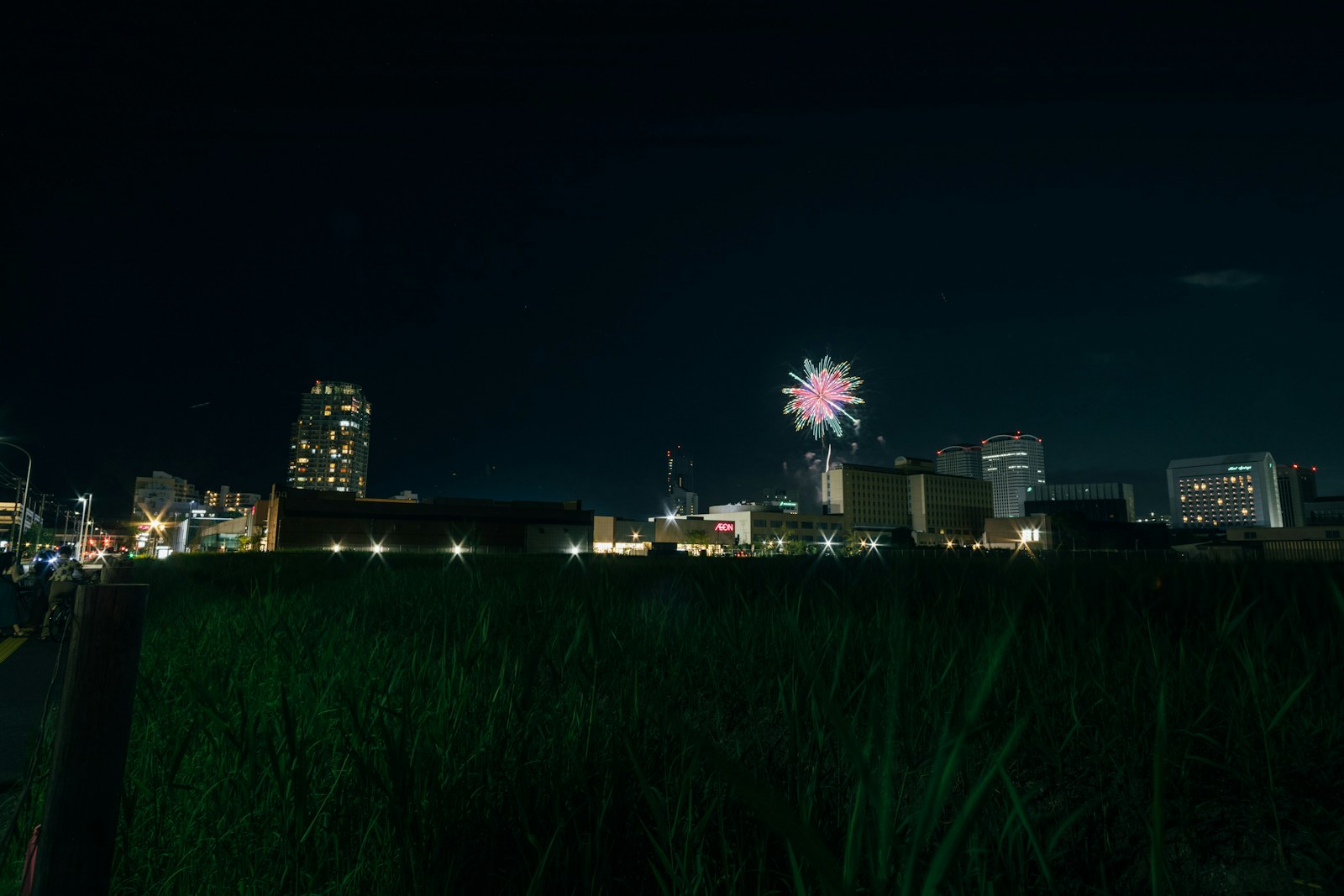 A distant firework above illuminated city buildings at night