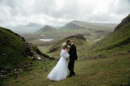 A bride and groom standing on a grassy hill