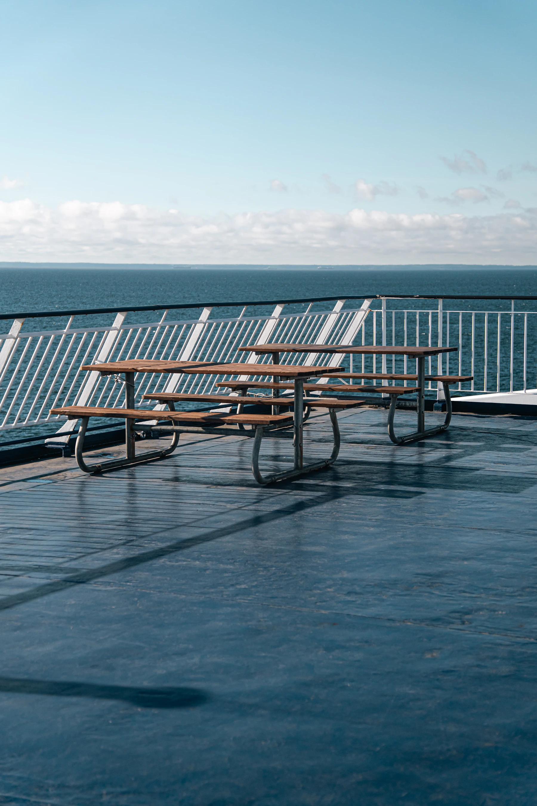 Wooden benches bolted to the open deck of a ferry, with the railing and open water beyond