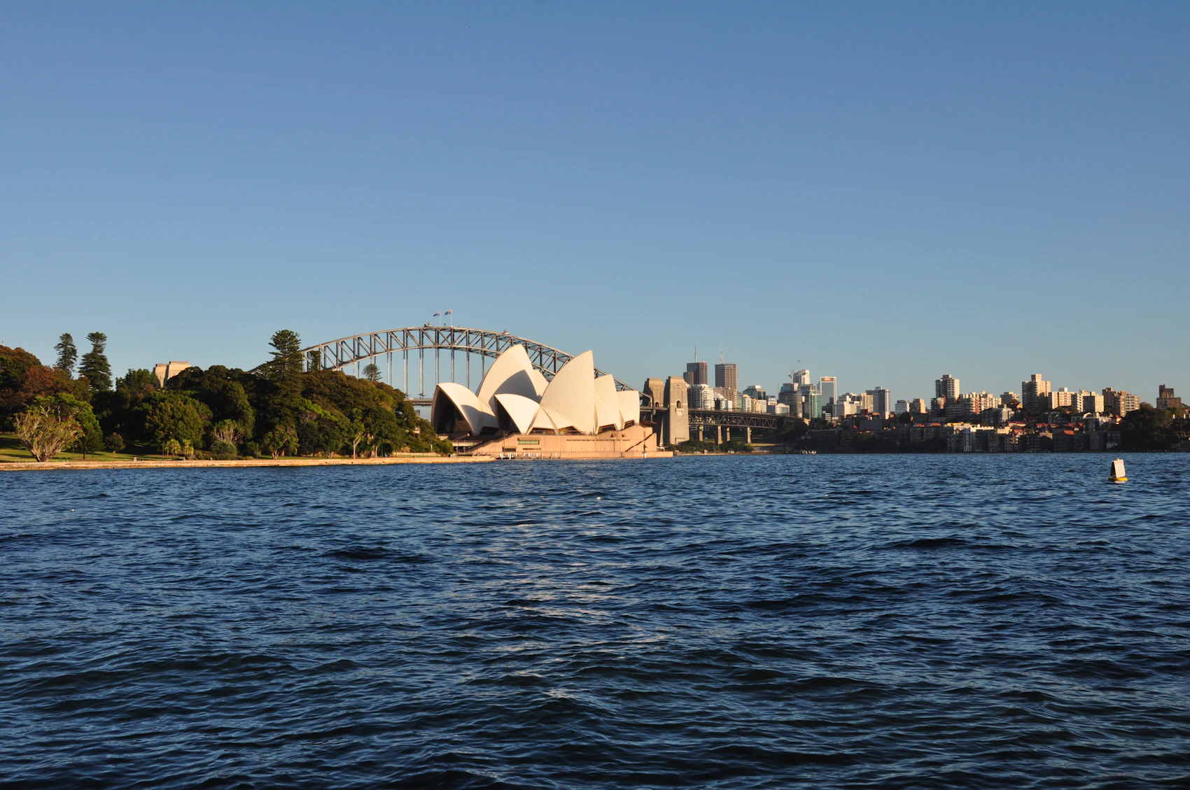 Sydney Opera House, Harbour Bridge and city skyline viewed across the water beside the Royal Botanic Garden