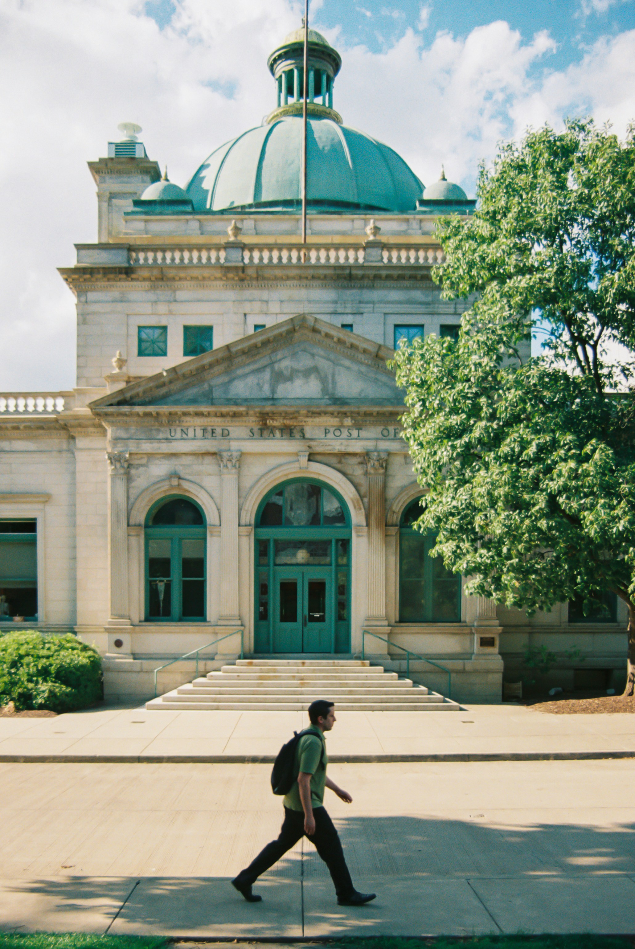 A man walking across a sidewalk in front of a building photo – Free ...