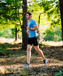 A man running through the woods in a blue shirt