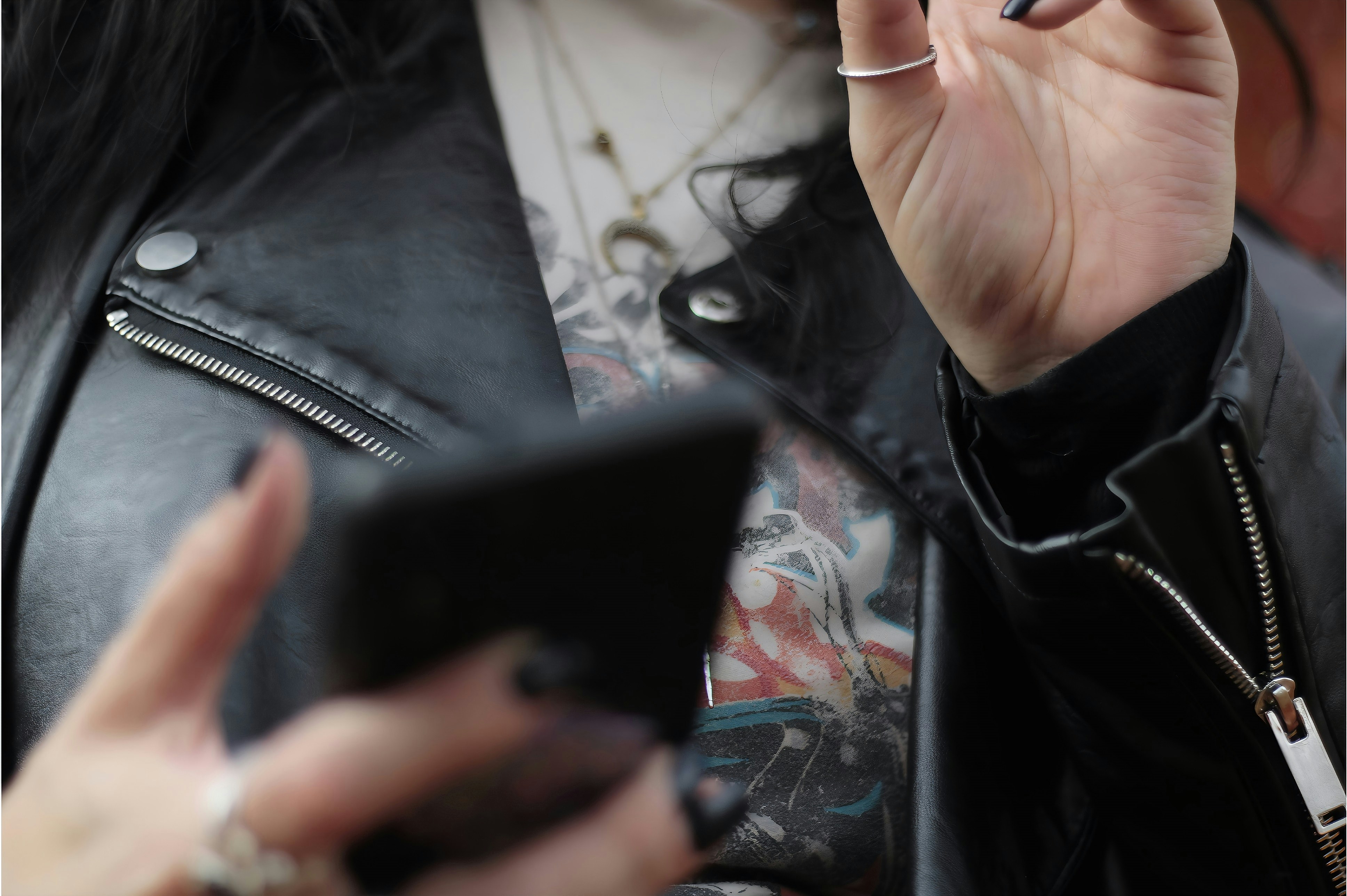 Person holding phone wearing leather jacket and talking