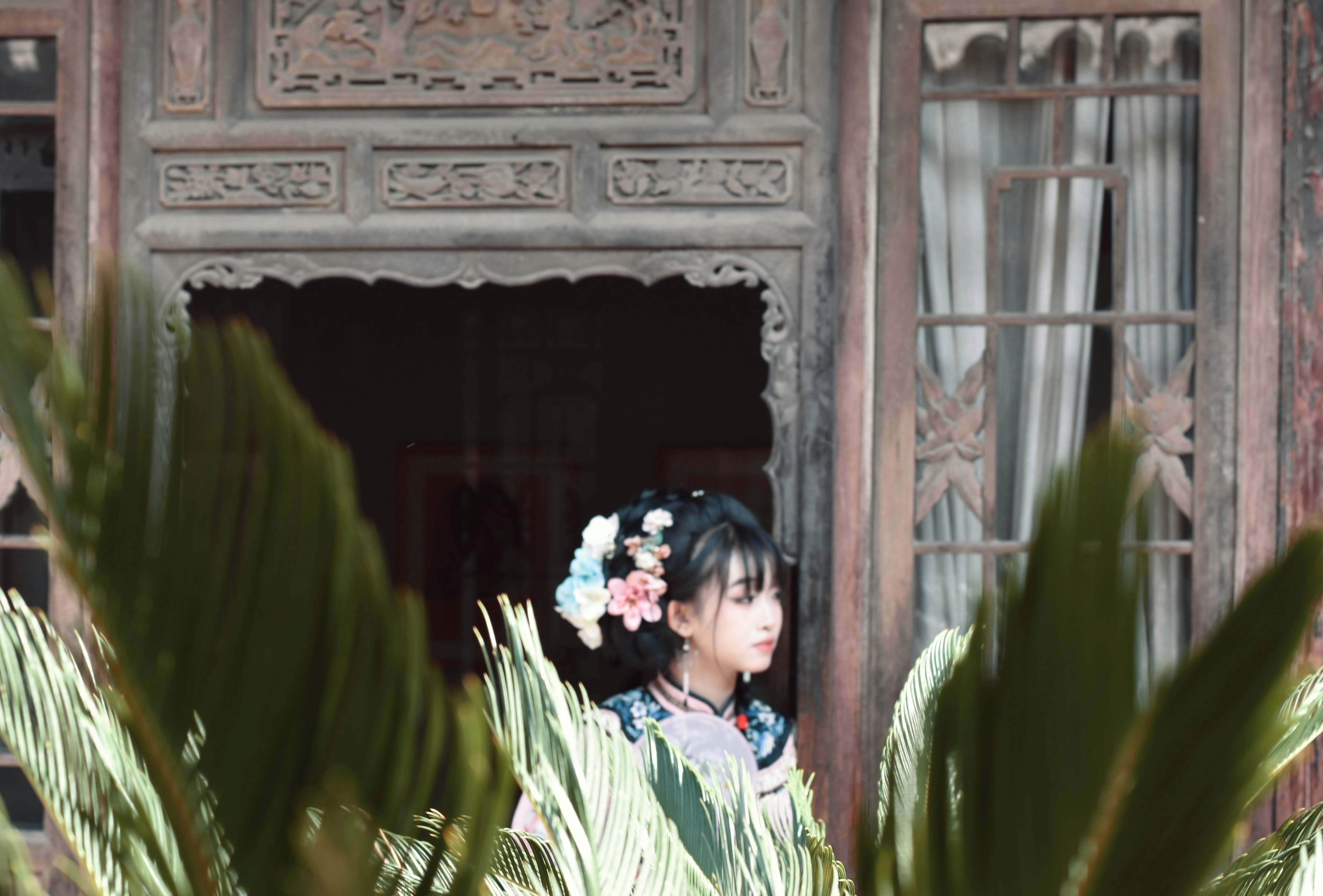 Uma mulher em pé em uma janela com uma flor no cabelo