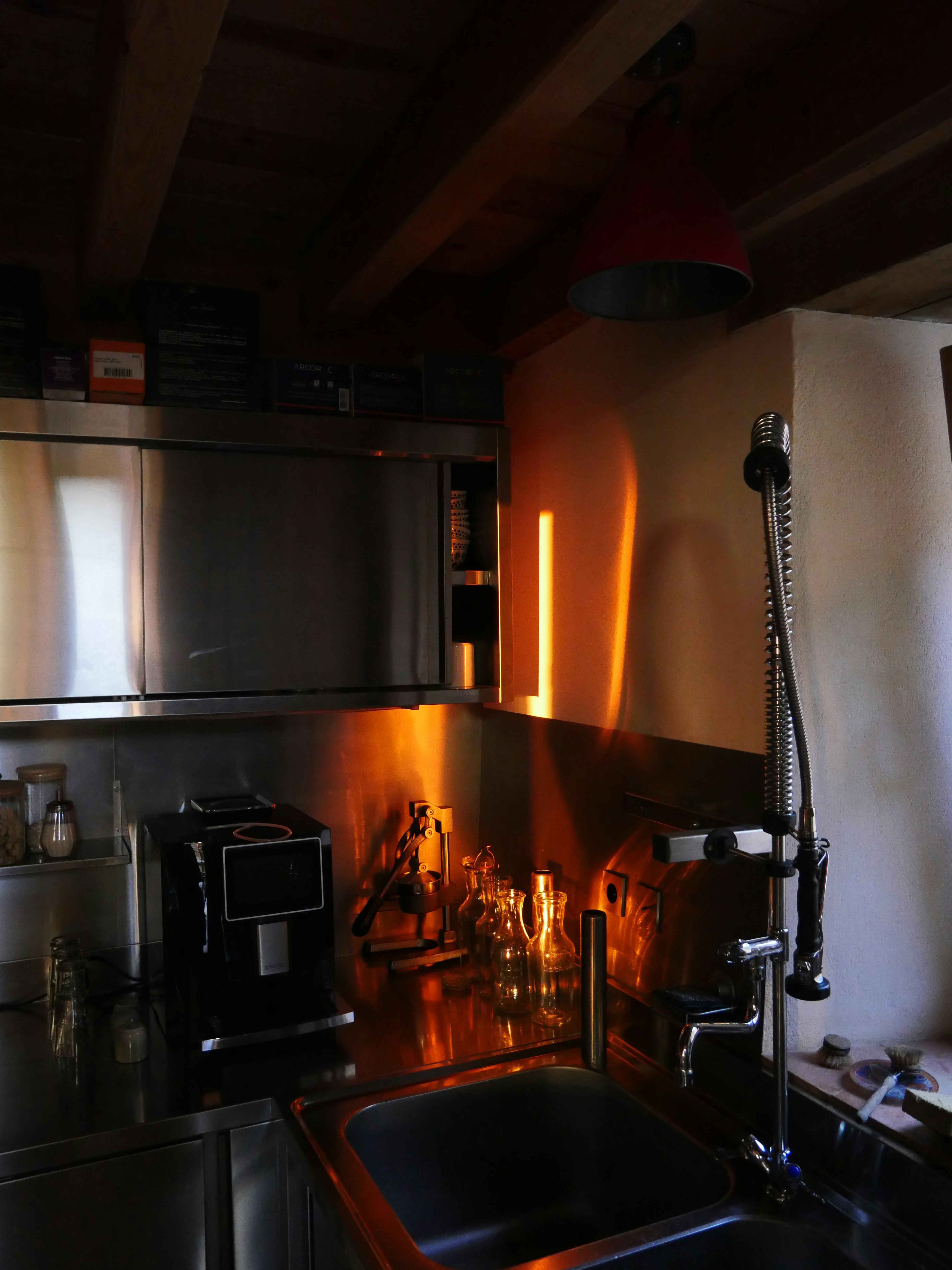 Coffee being poured into glass, warm golden amber tones, bright overhead lighting, airy kitchen setting