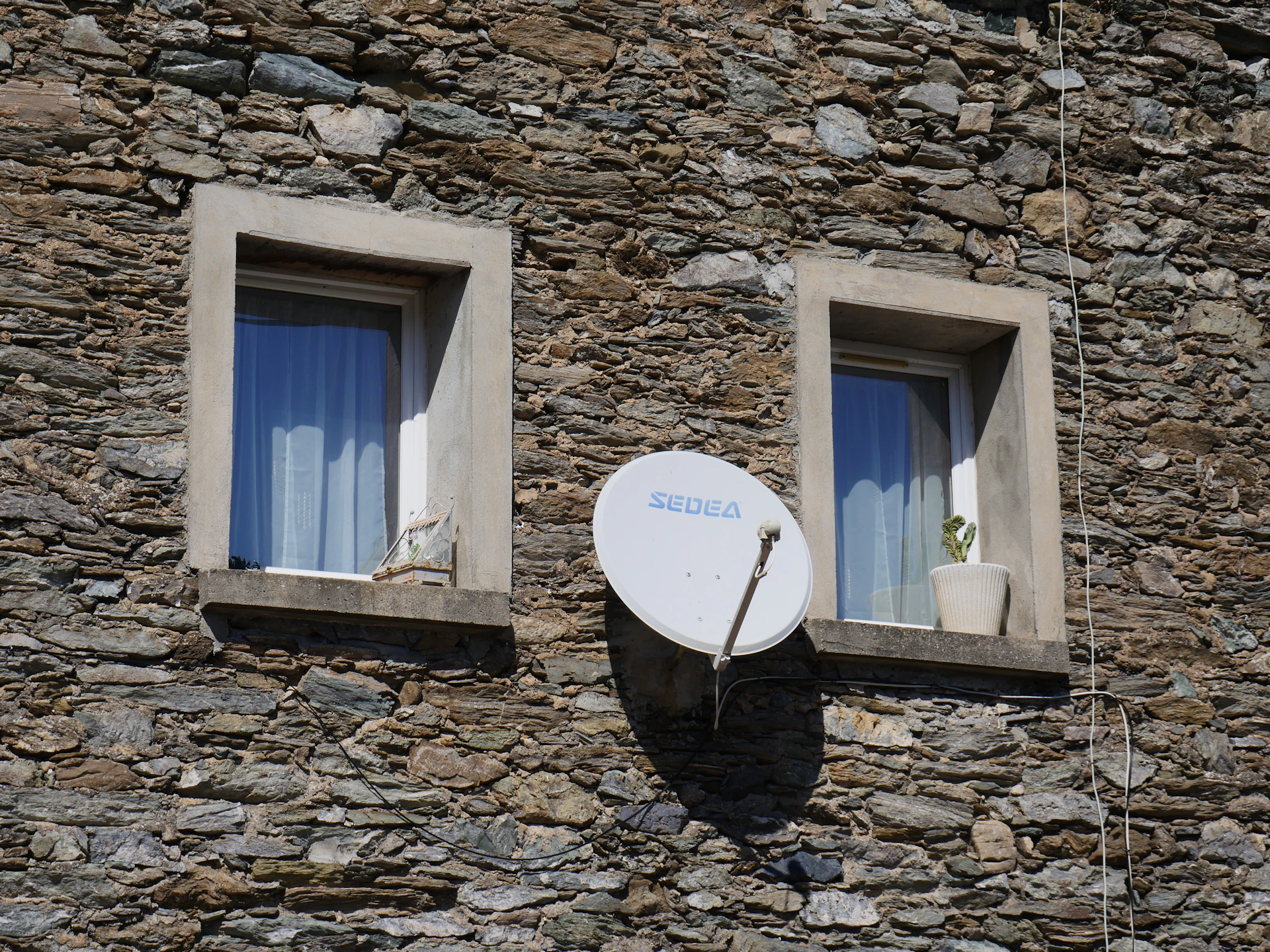 A satellite dish mounted to the side of a stone building