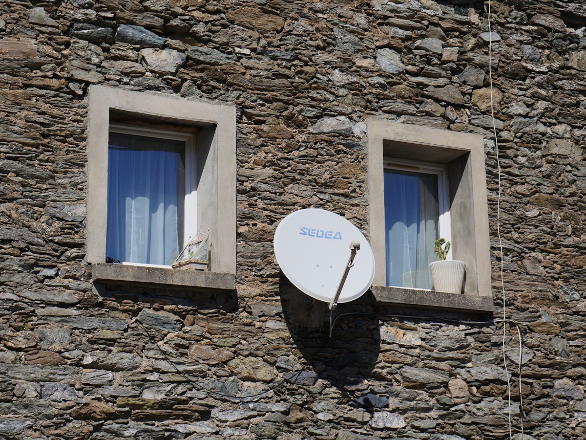 A satellite dish mounted to the side of a stone building