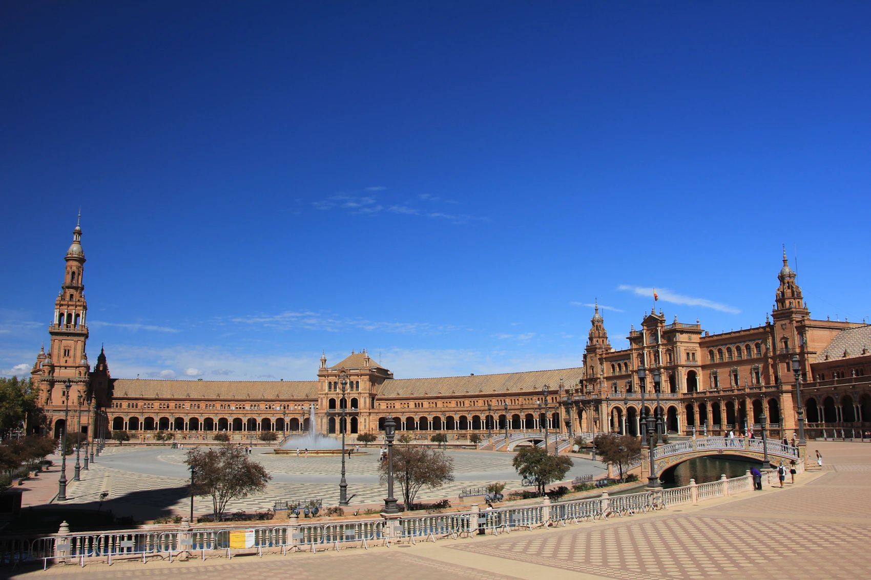 The sweeping arc, canal and tiled bridges of Plaza de España beneath a blue Seville sky