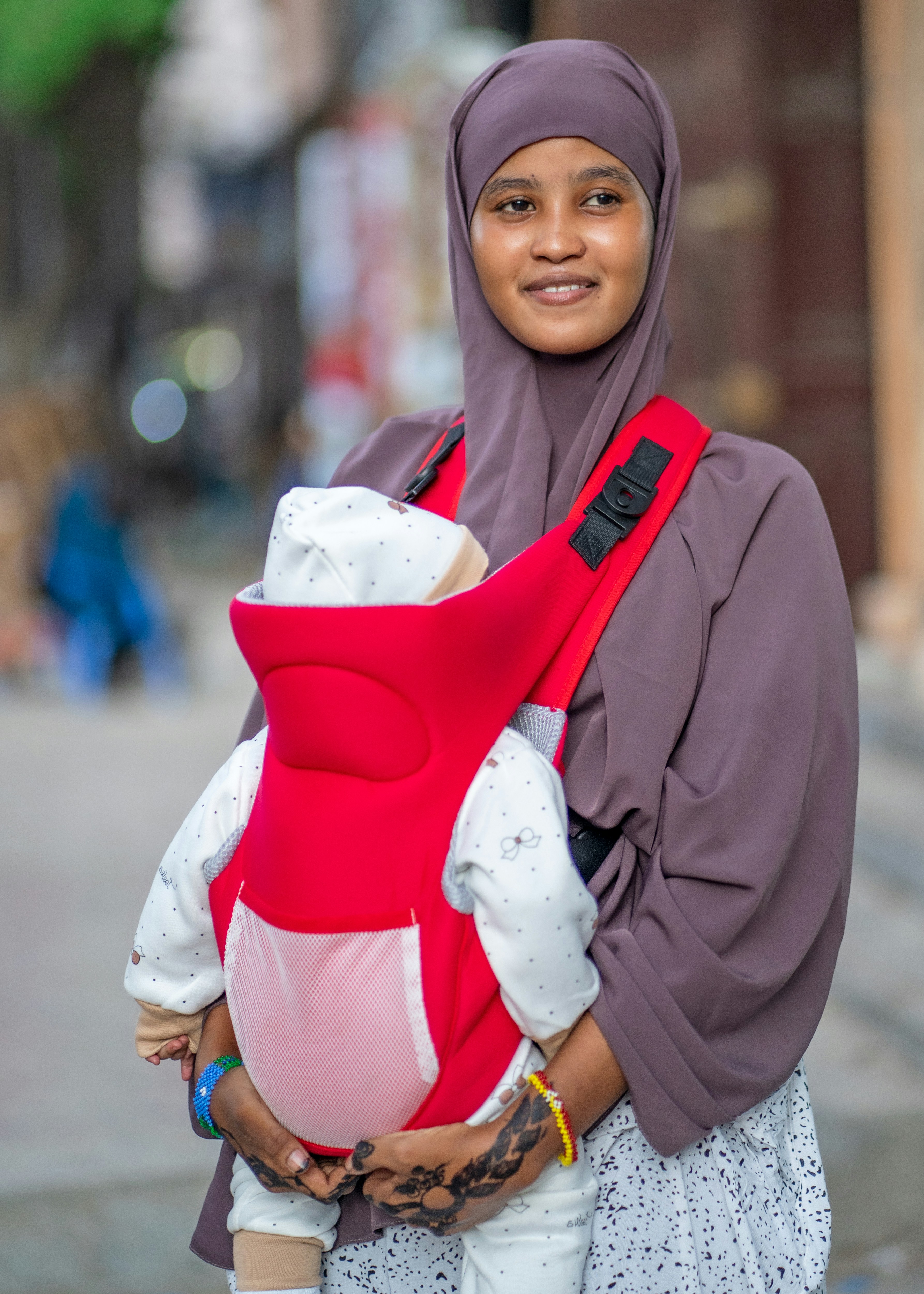 A woman in a hijab holding a baby in a sling