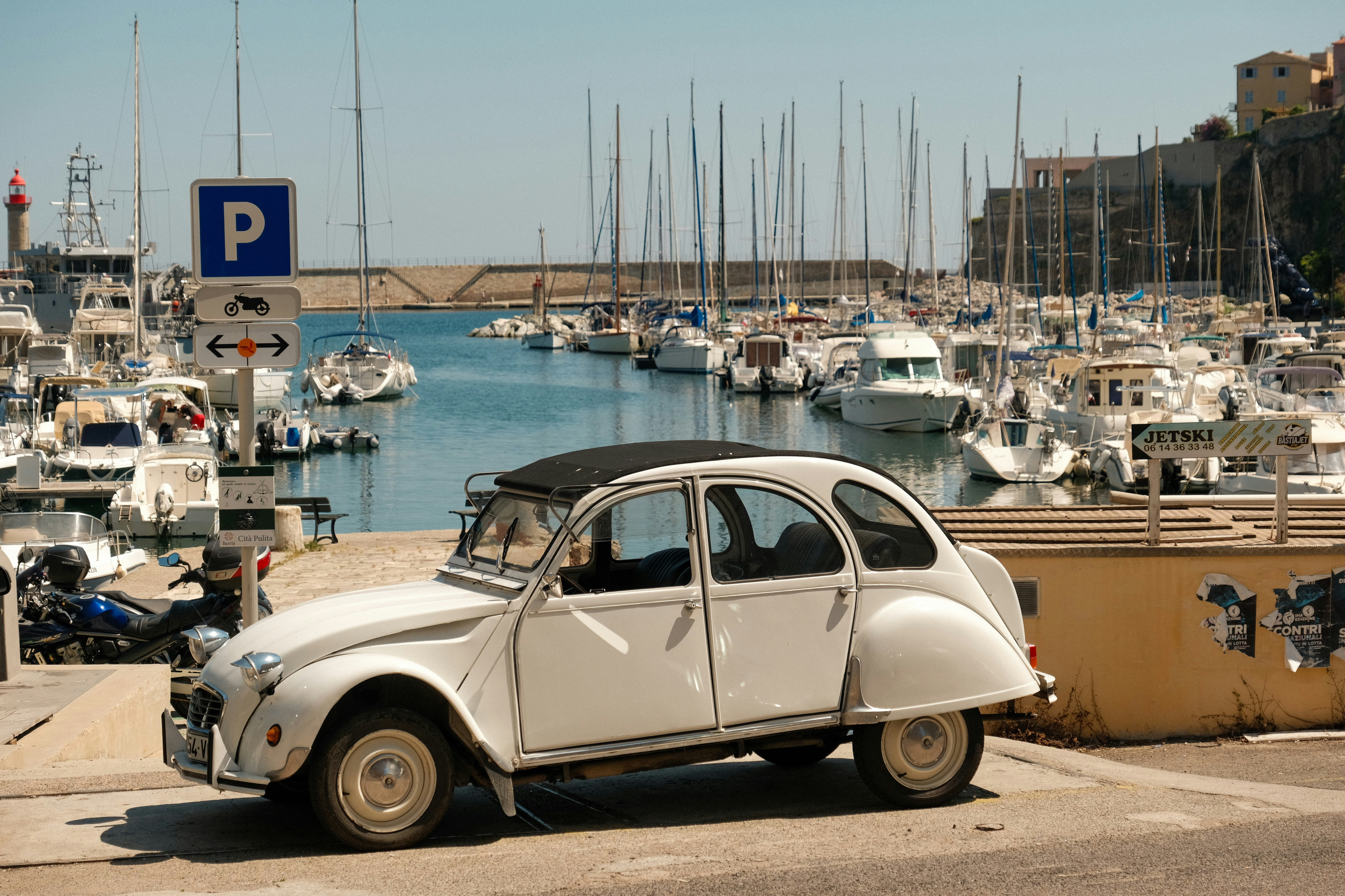 A white car parked in front of a marina filled with boats