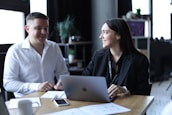 A man and a woman sitting at a table with a laptop, collaborating on a business project.