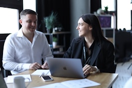 A man and a woman sitting at a table with a laptop, collaborating on a business project.