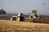 Two tractors are plowing a field of crops