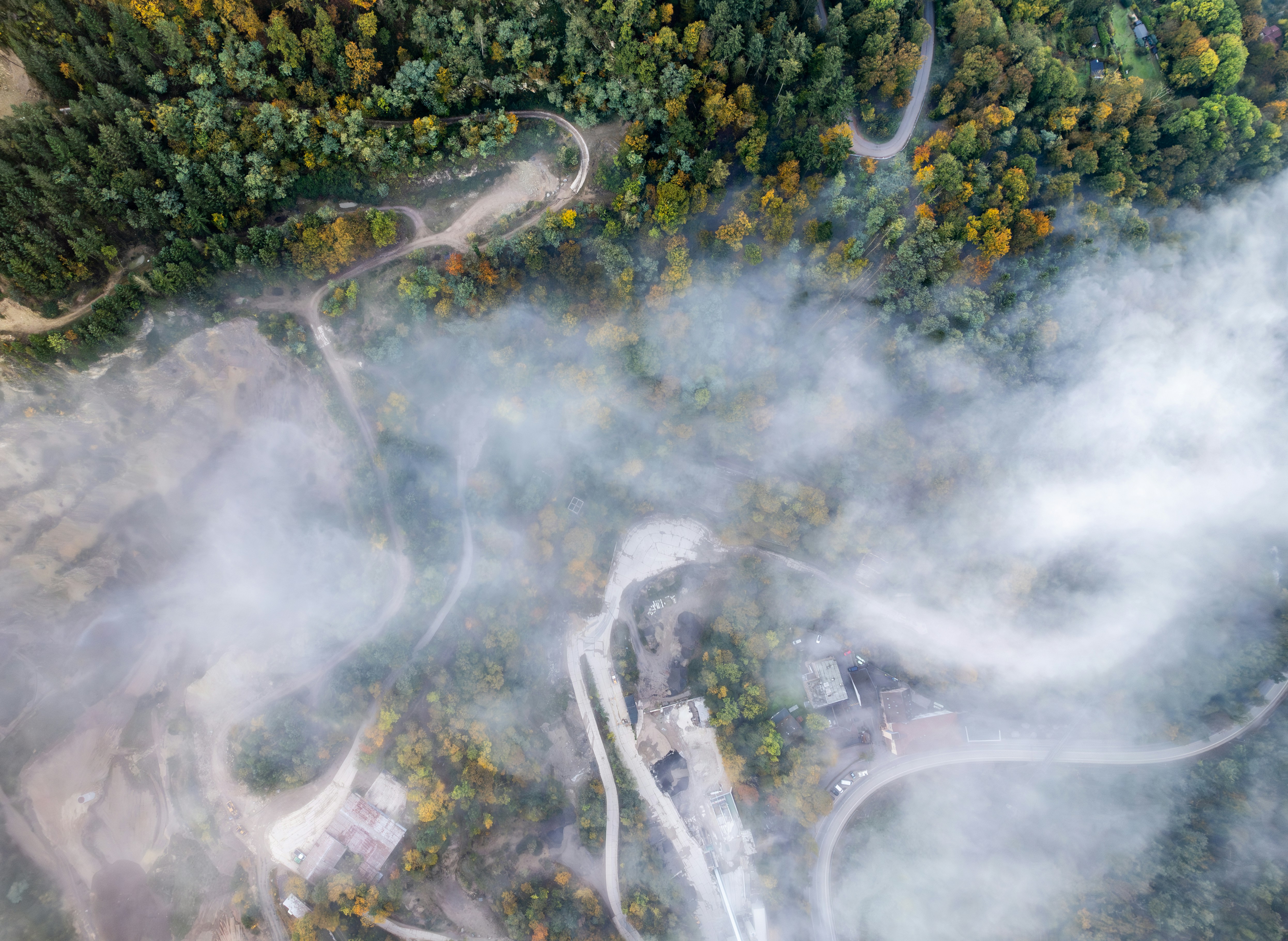 Aerial view of a dense, green forest with smoke rising in the distance, indicating a crash site.