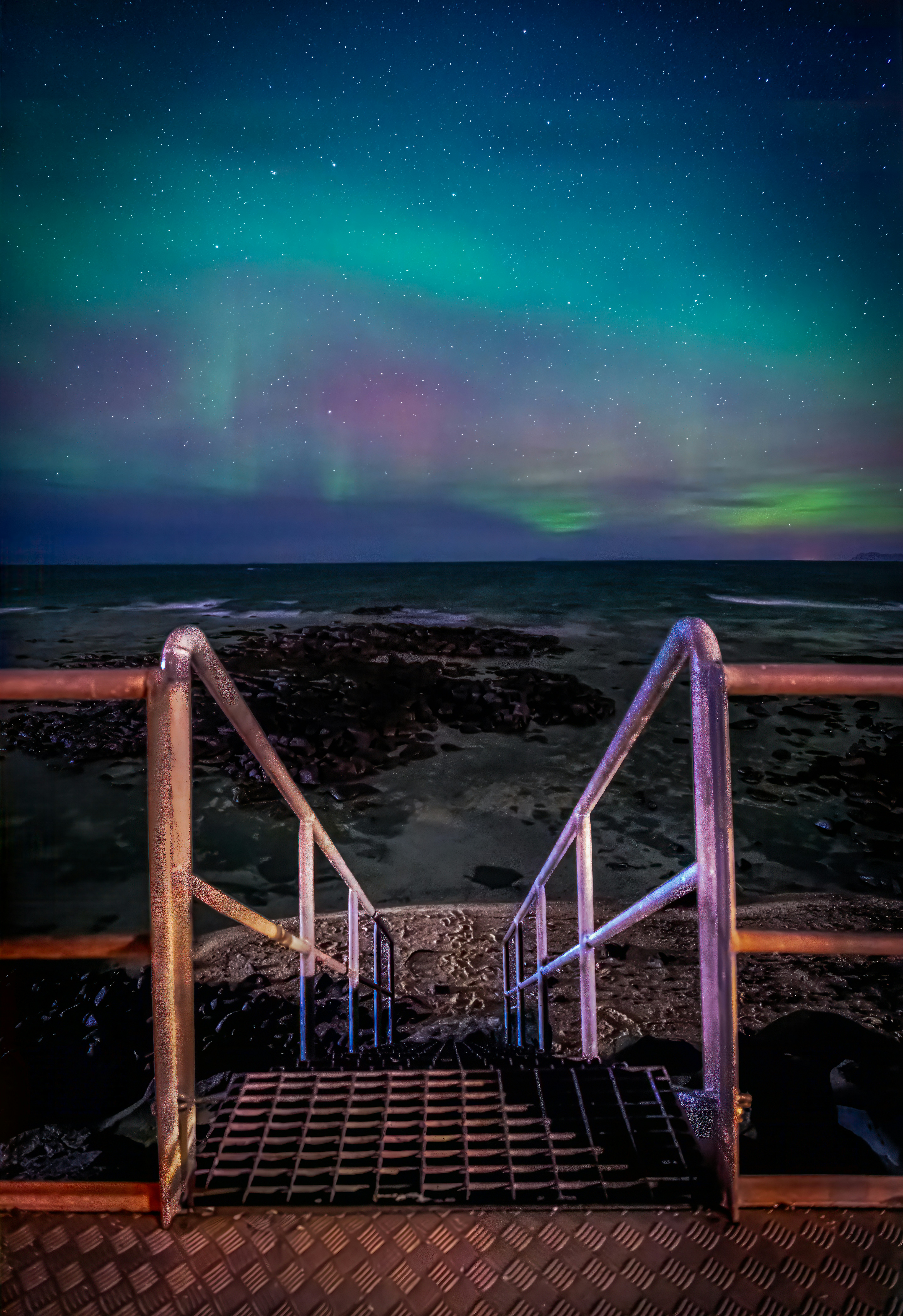 A stairway leading to the ocean under a green and purple sky