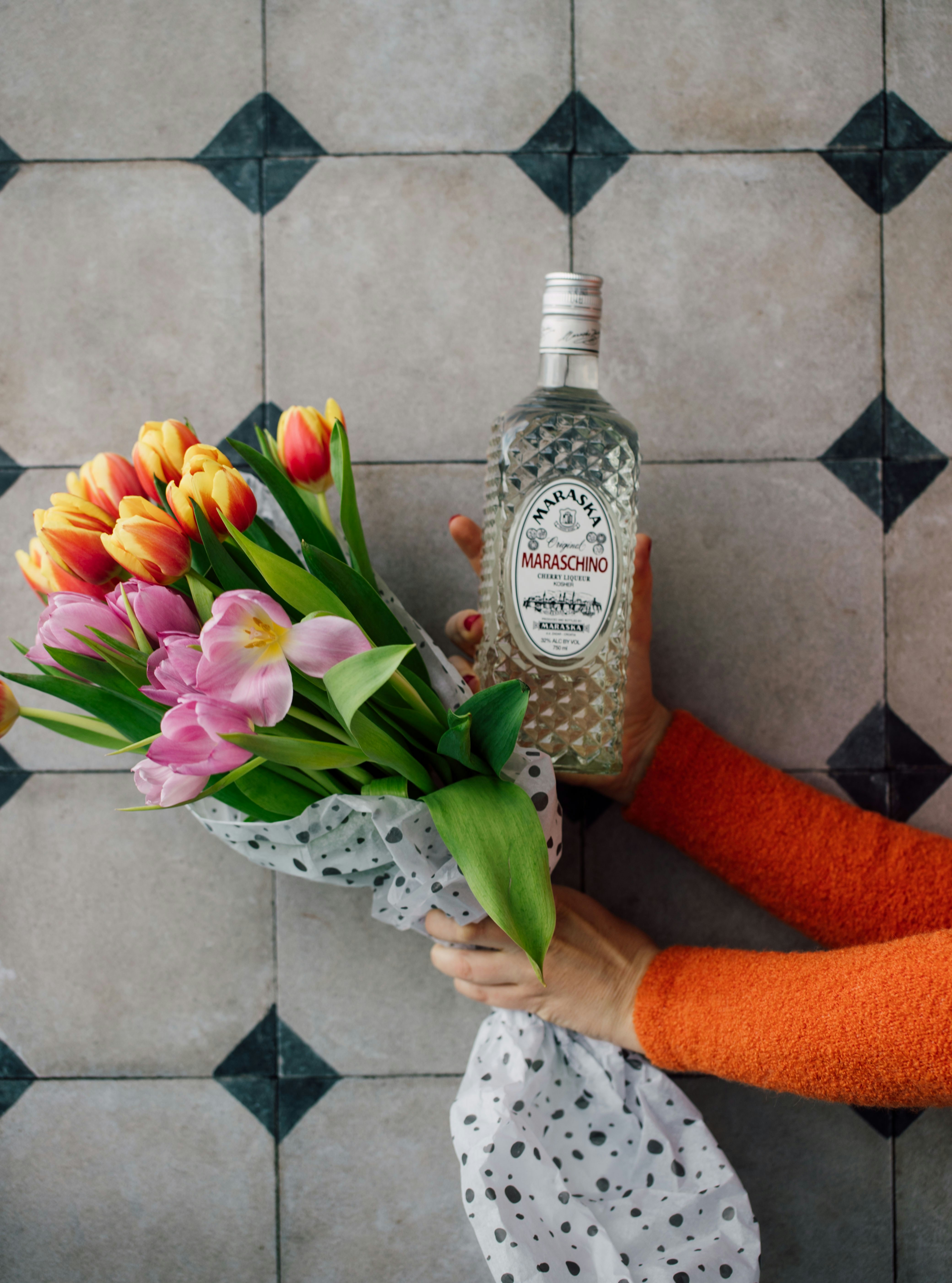 A woman holding a bouquet of tulips and a bottle of gin