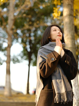 A woman standing in front of a tree with her hands together