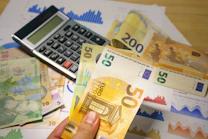 A person holding a bunch of money next to a calculator