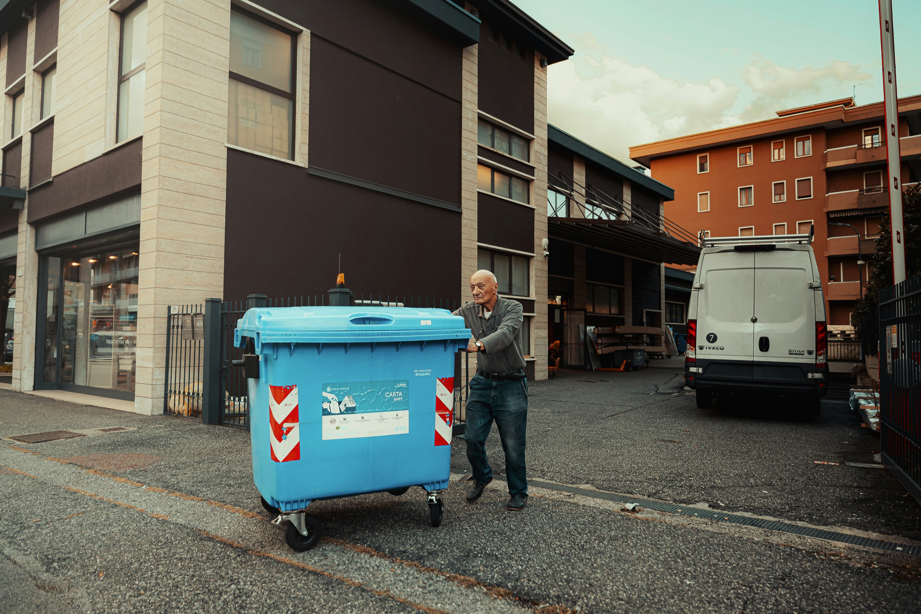 Un uomo che spinge un bidone della spazzatura blu lungo una strada